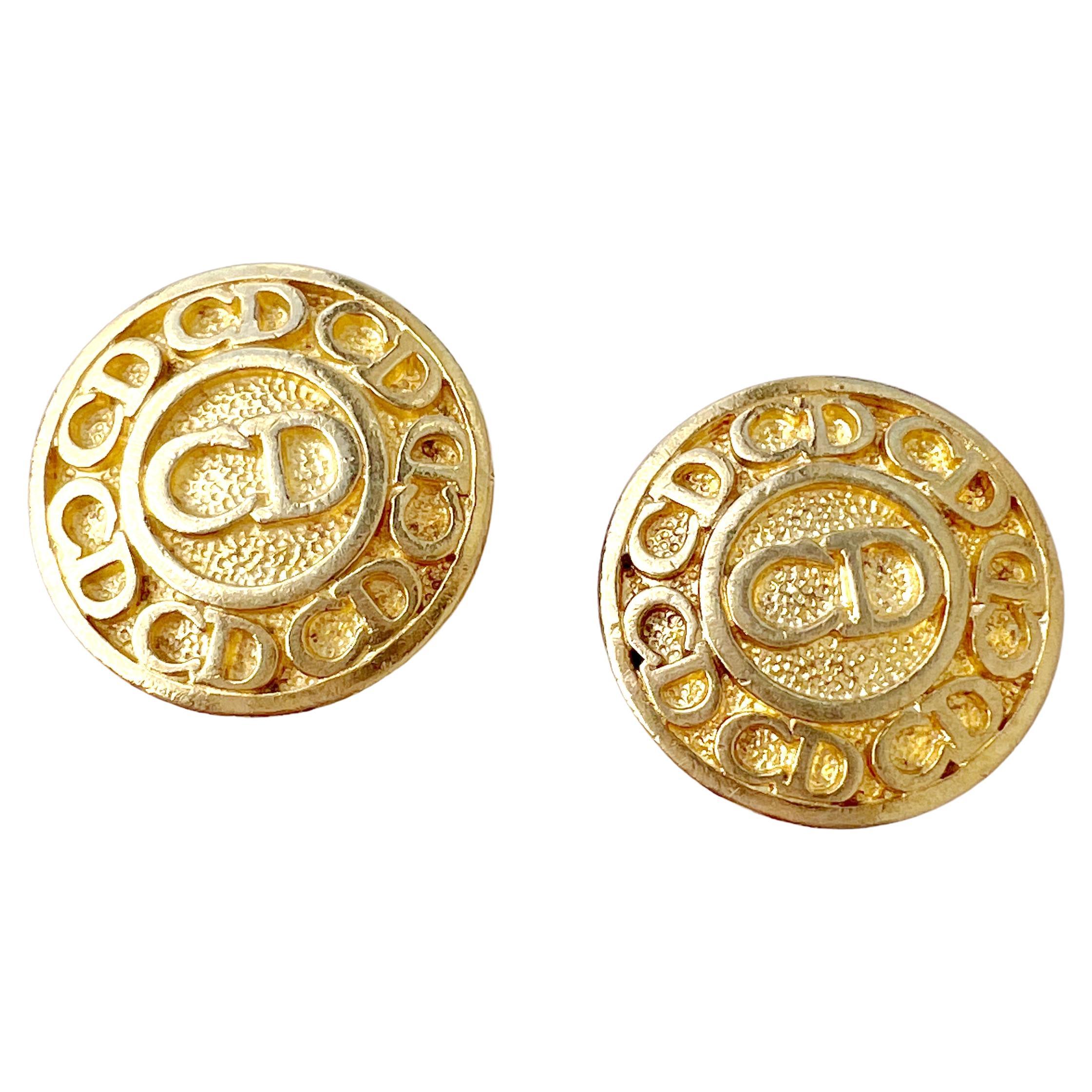 Vintage 1990s Christian Dior logomania-style medallion earrings in gold plate.  These heritage clip on earrings feature the Dior signature repeated CD logo in high shine over a textured background.   The earrings measure just under an inch in