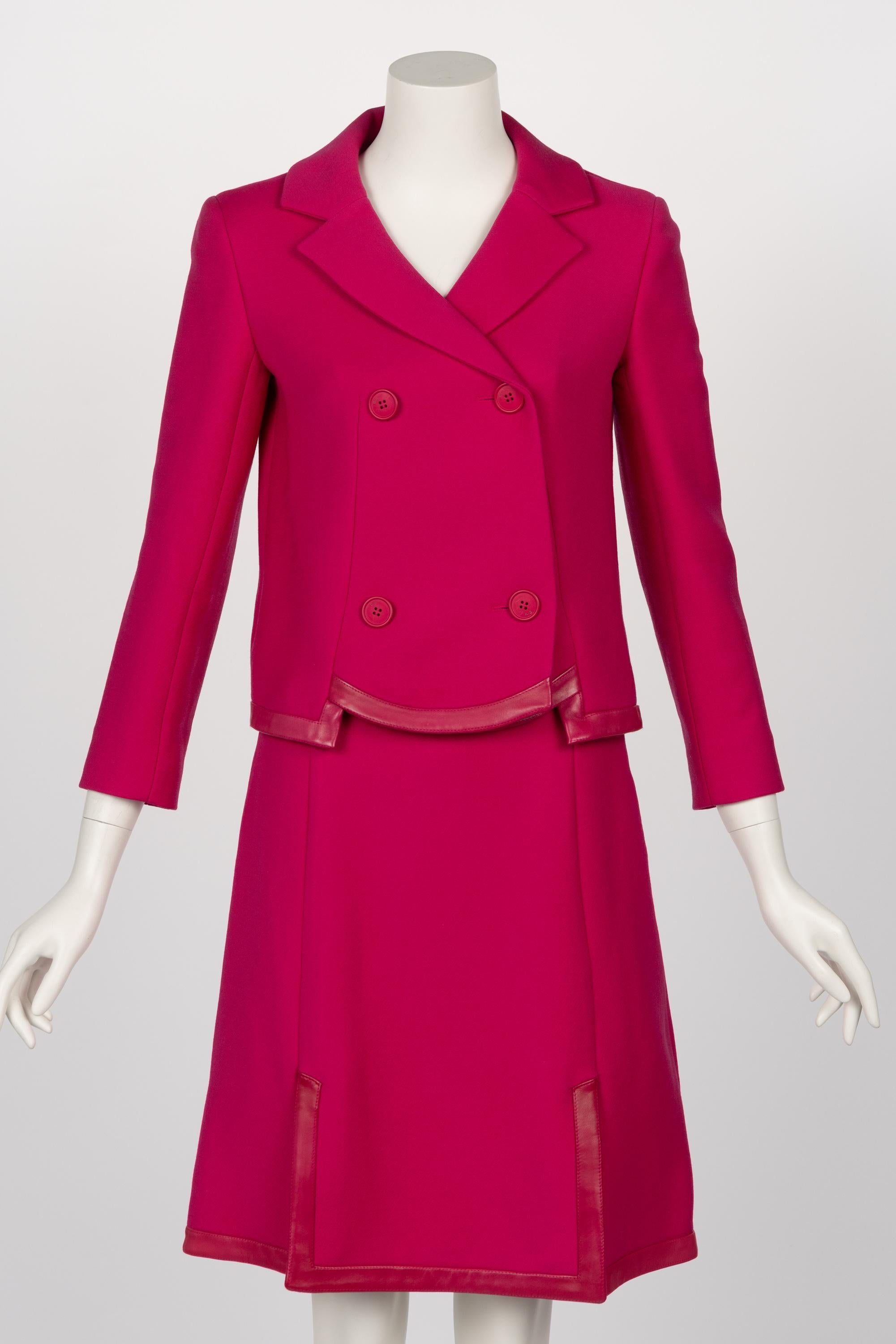 This vintage Christian Dior skirt suit from the Galliano era is crafted from a striking pink wool and features a double-breasted jacket with wide, notched lapels and decorative buttons. The jacket’s leather trim at the hem adds a contemporary,