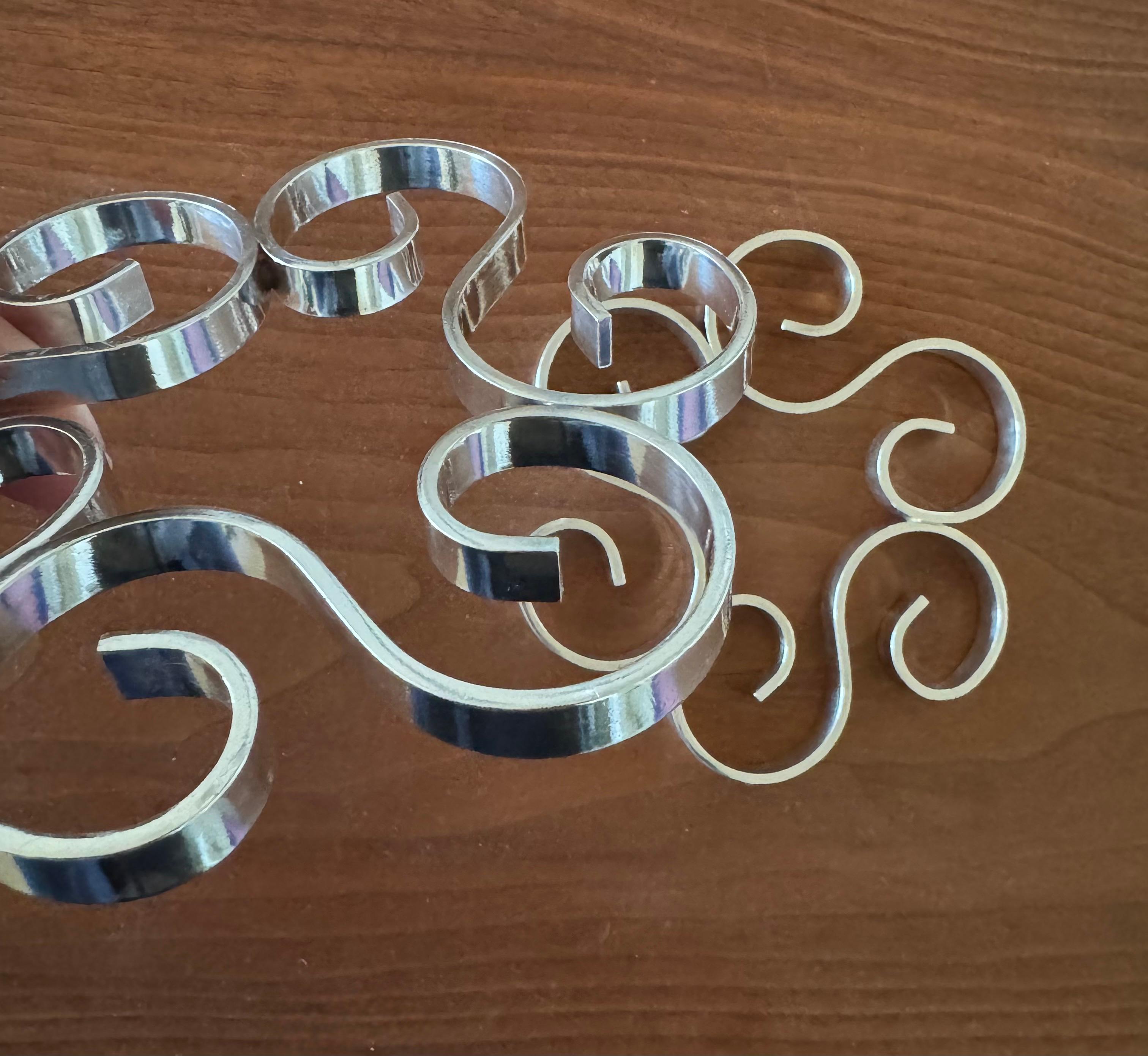 A vintage pair of arabesque trivets from the original Christofle of Paris line of cast Gallia metal and silver plated luxury goods offered between 1900-1937. Each trivet consists of three scrolled S-curves and is stamped Gallia / FRANCE alongside