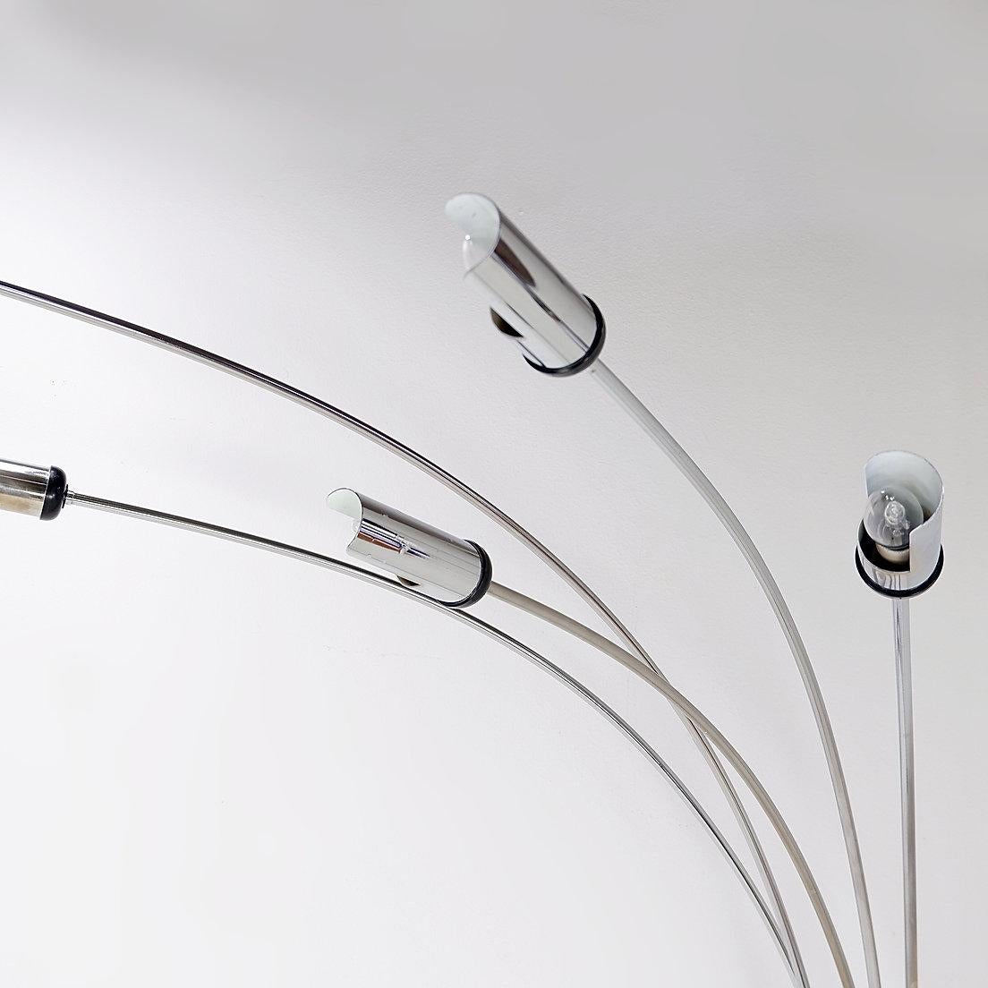 Lampada da terra Gerbe con cinque bracci luminosi ad arco in metallo cromato, con coprilampada cilindrici su una base rettangolare in ghisa nera ricoperta da una lastra di metallo cromato. attribuita a Reggiani. 
Anni Settanta - Vintage -