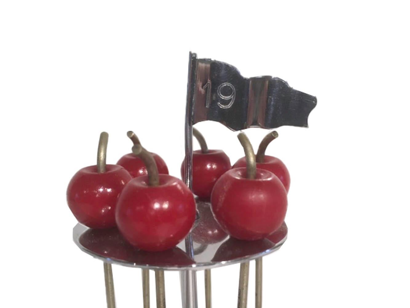 Vintage golf themed chrome cocktail picks. The chrome picks with red Bakelite apple-form tops hang through a pierced disk raised on a 19th hole golf flag.