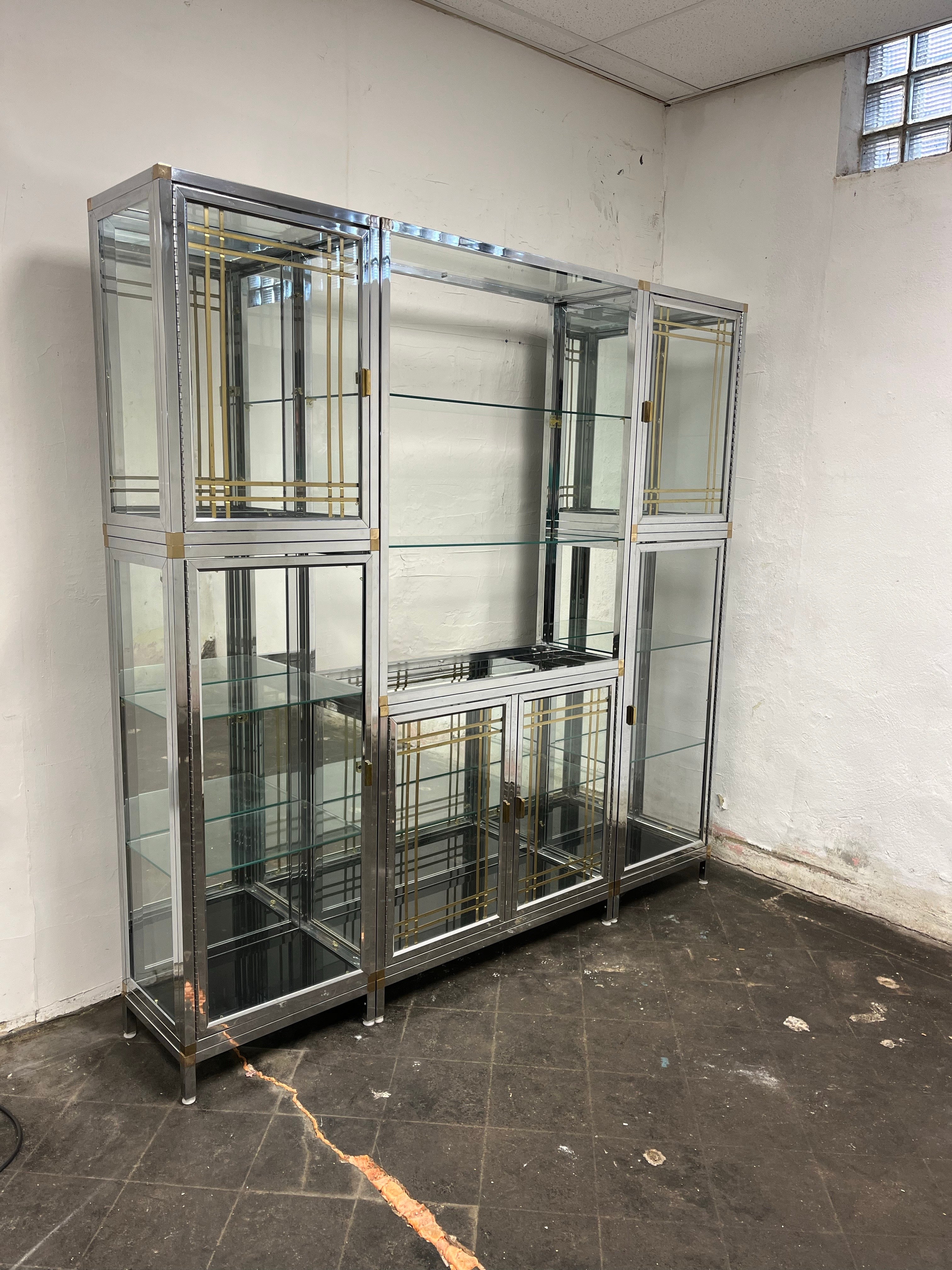 This gorgeous display case is made up of 5 chrome, brass, glass and mirror case pieces and 1 mirror back open shelf. Bottom case pieces have black glass on the bottom. Each piece reflects the light and the back of the objects inside beautifully. The
