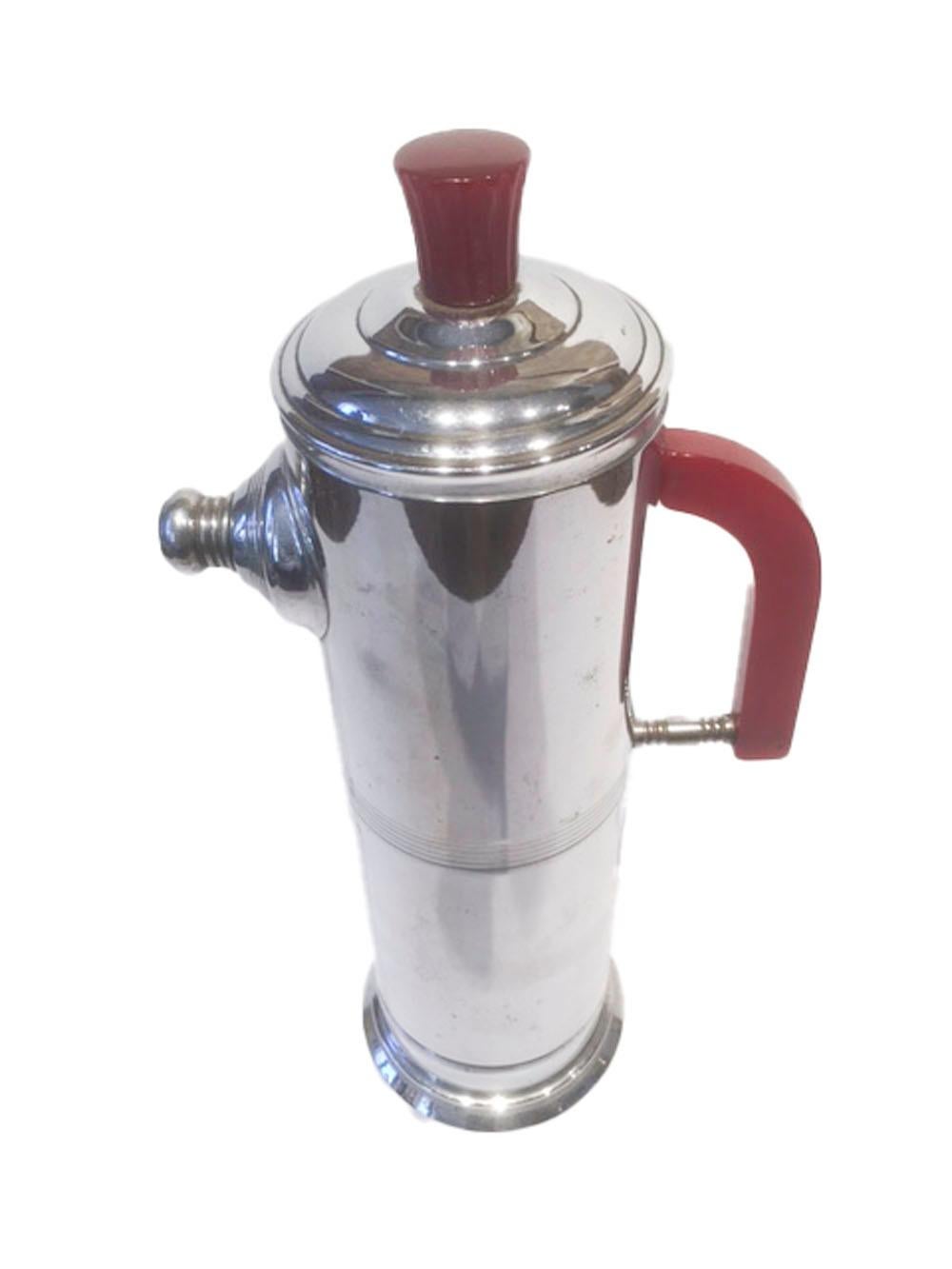 Art Deco chrome and red Bakelite cocktail shaker of cylindrical form. The domed, stepped lid with flared and ribbed Bakelite knob sits atop the cylindrical body with Bakelite handle and central ribbed band rising from a stepped foot.