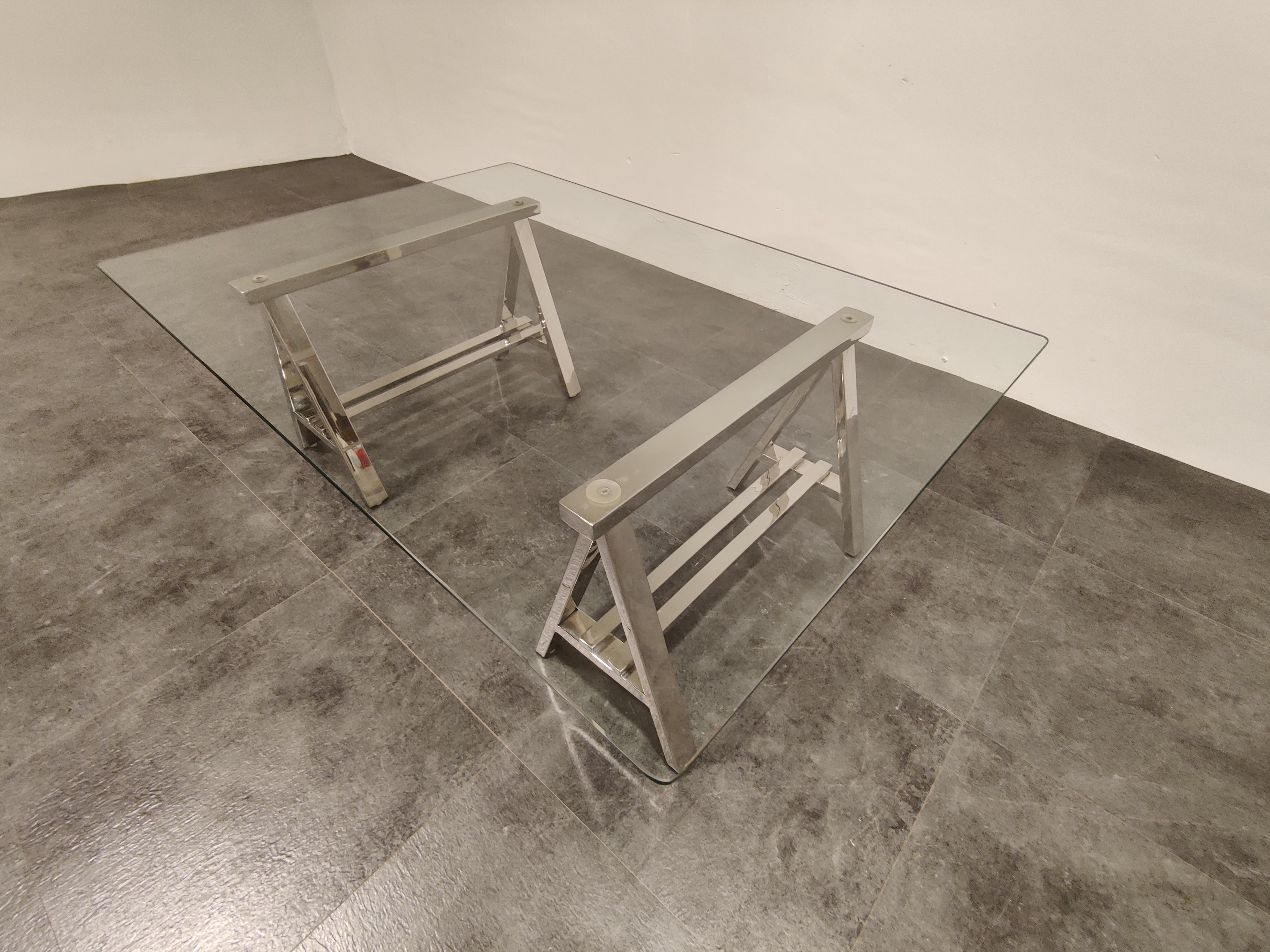 Unique coffee table consisting of two chrome trestle and a clear glass top.

Acquired in the 1980s at Roche Bobois, a French top end furniture retailer.

Hollywood Regency style.

Very good condition.

1980s, France

Dimensions:
Height