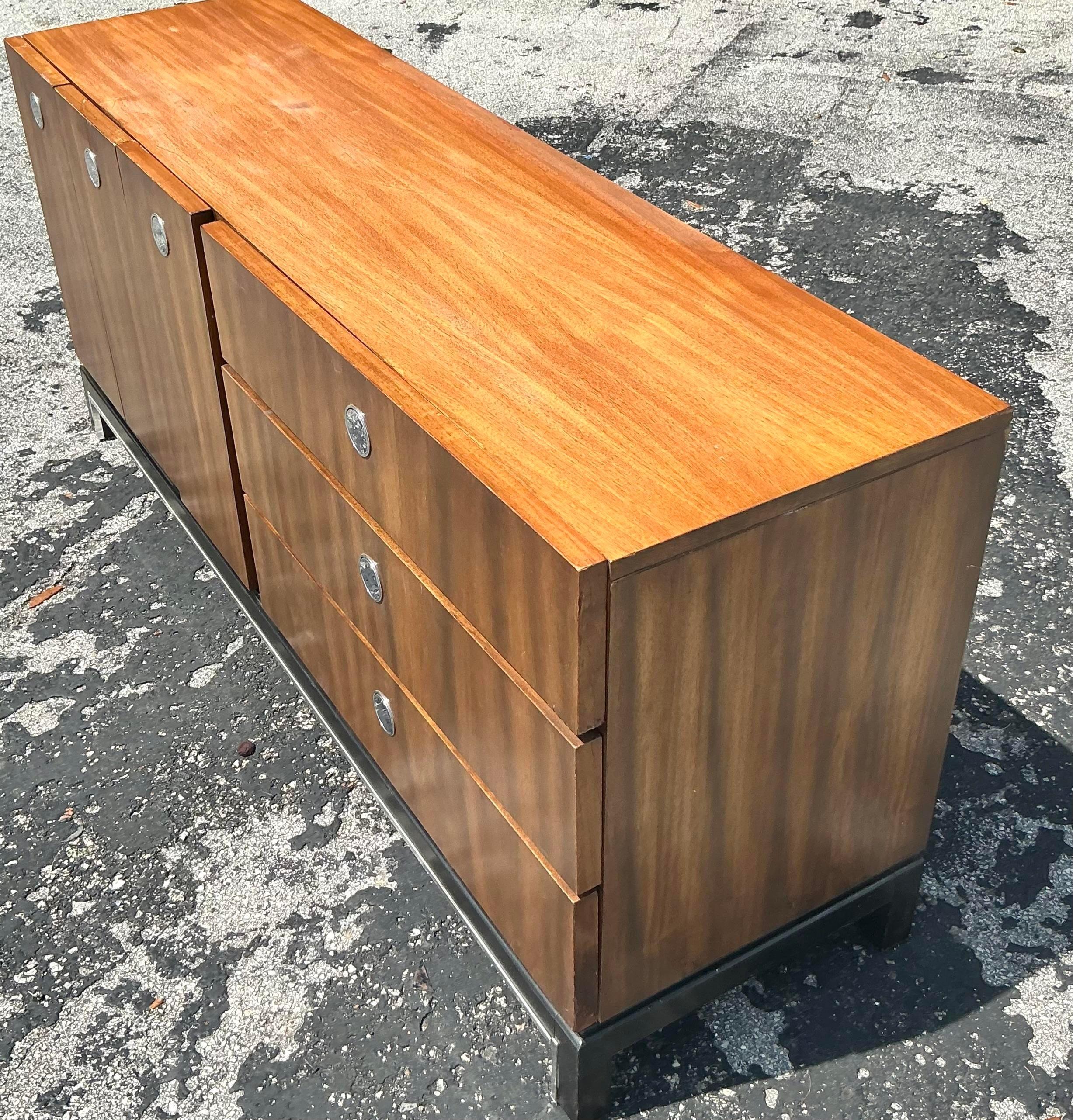 Add sleek, retro flair to your space with this vintage MCM chrome-trimmed dresser. Featuring clean lines and a bold contrast between the rich wood finish and polished chrome accents, this piece perfectly captures mid-century modern design. With