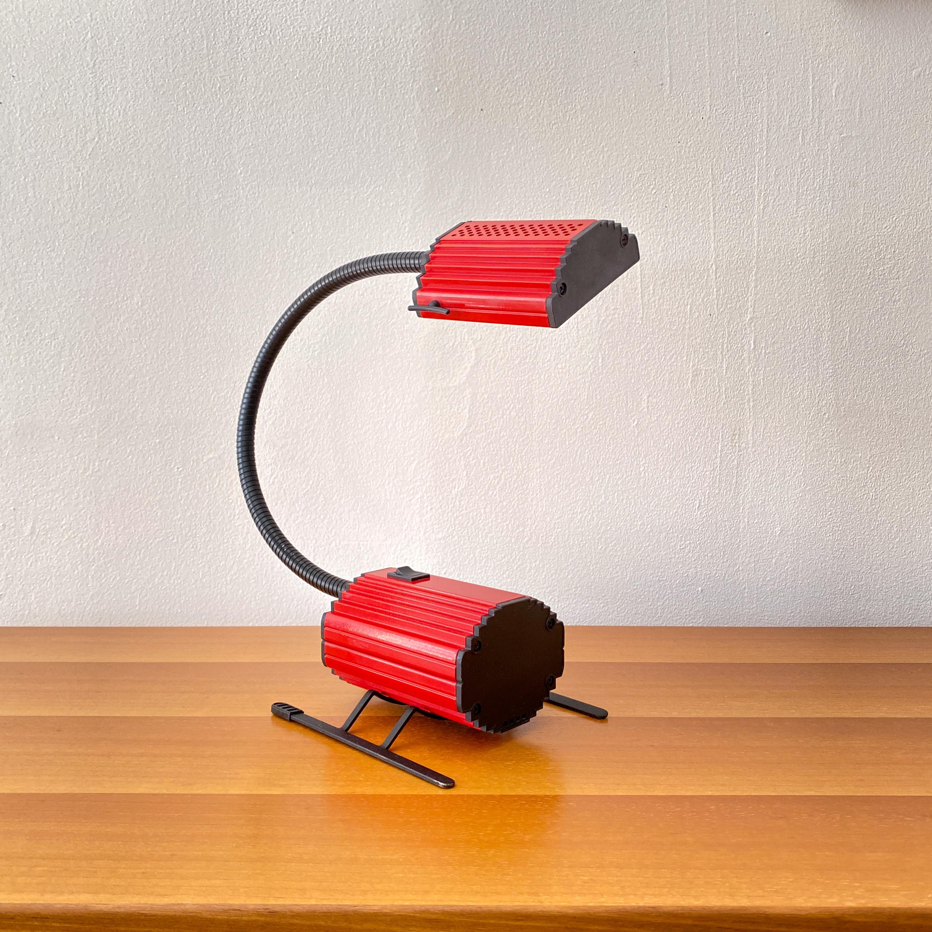 A vintage table lamp design in 1983 by Enzio Didone for Arteluce and made in Italy. The lamp is halogen with a red painted metal hood and and body. The end caps on the hood and body are black plastic, the black painted goose neck it flexable metal.