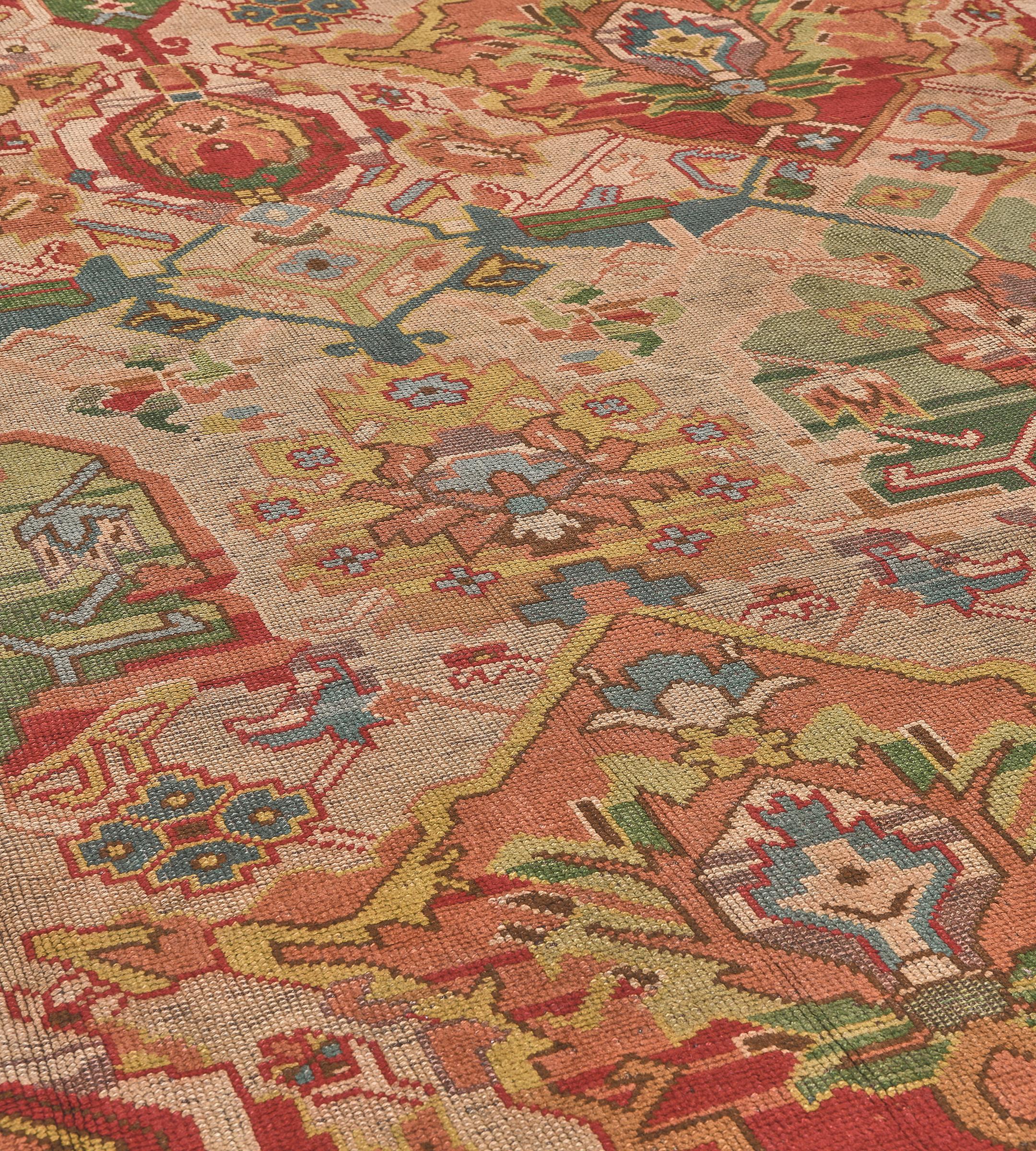 This vintage, circa 1900, hand-woven Irish Donegal rug has a dusty-pink field with an overall design of polychrome angular serrated vine with three vertical columns of polychrome bold shield panels each containing a central floral rosette and an