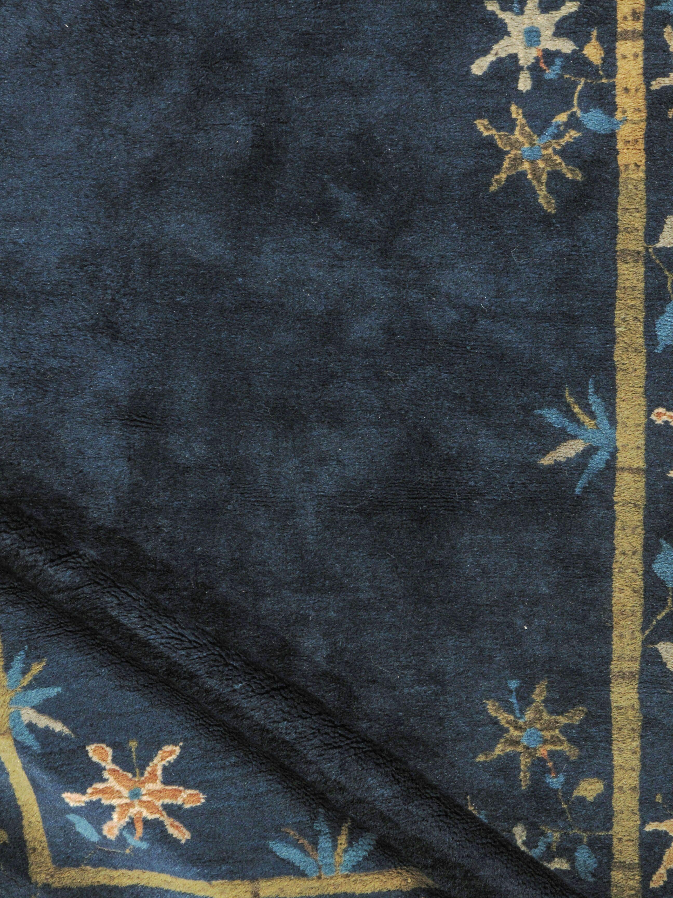 4' x 6'7. Maravilloso ejemplo de alfombra china de estilo Art Déco tejida hacia 1920 con un fondo liso azul marino rodeado de flores y estrellas en una variedad de colores suaves y apacibles.