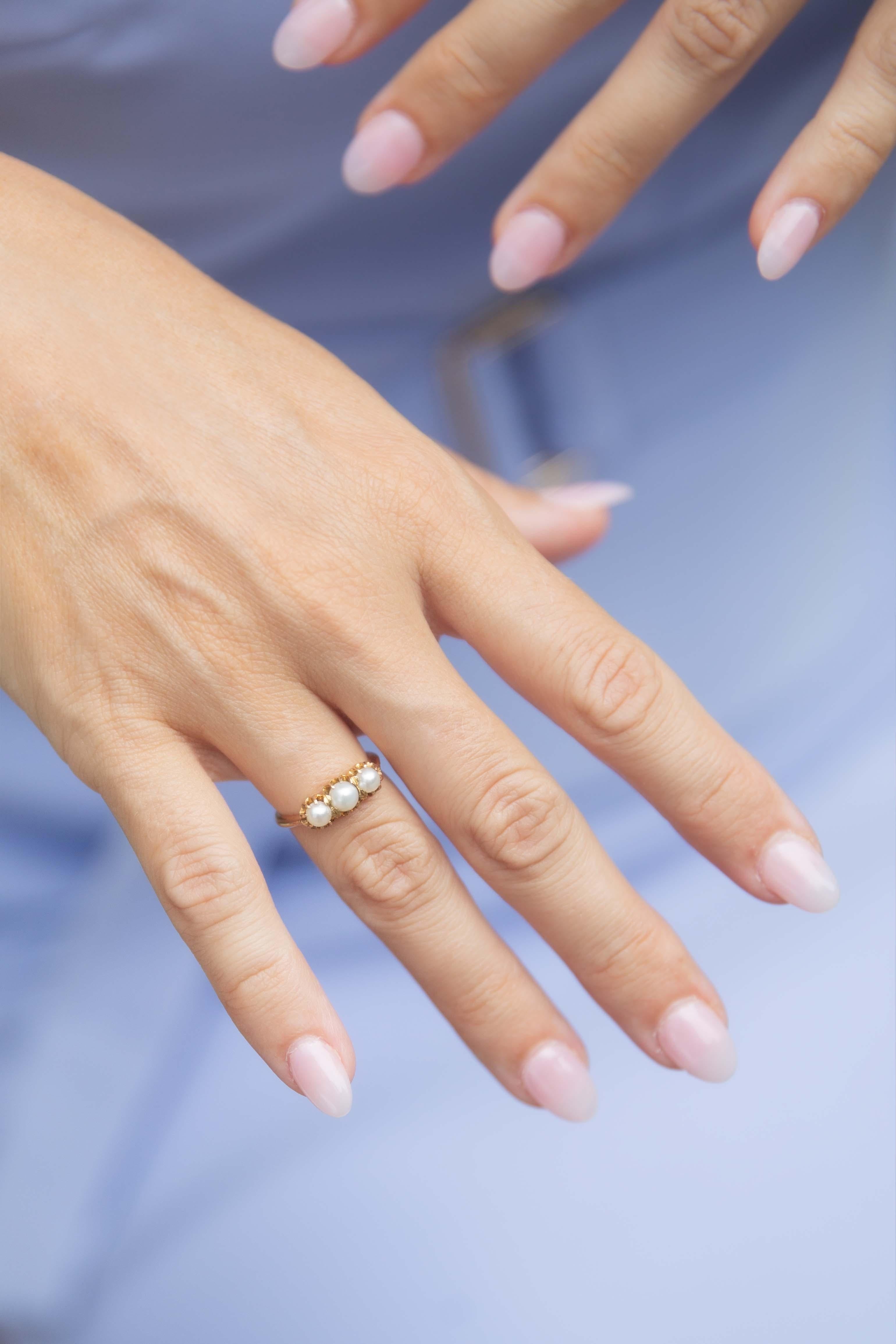 Glissant dans le crépuscule de l'élégance, la bague à trois pierres Ginevra Pearl Antique des années 1930 scintille d'une danse de lumière opulente. Chaque perle lustrée, bercée dans de l'or jaune 15 carats, murmure des histoires d'amour et de