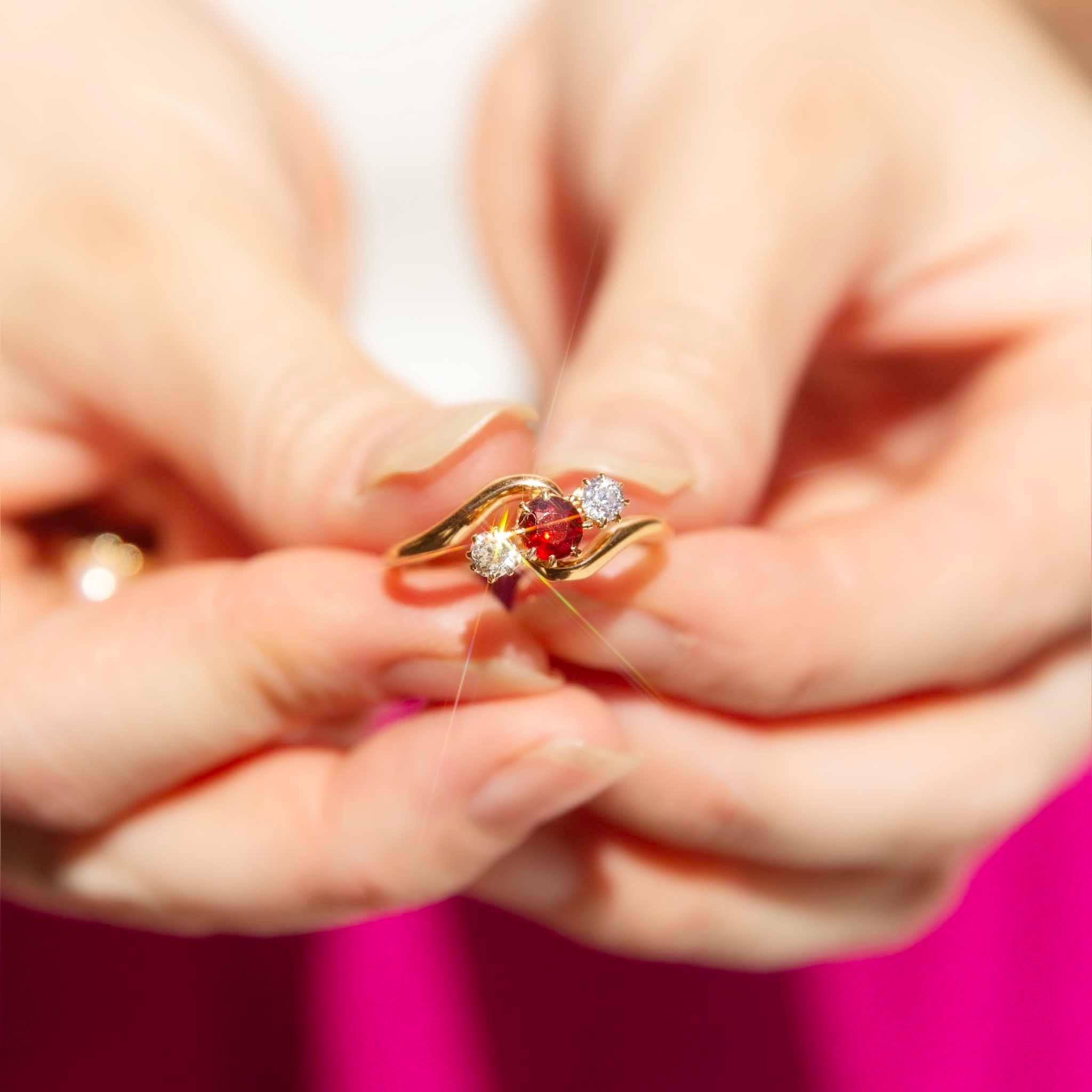 Elegance and refinement come together wonderfully in The Brielle Ring. An enchanting one almandine garnet flanked by two shimmering round diamonds, all set carefully into a trio of claw settings held in the loving embrace of gleaming crossover