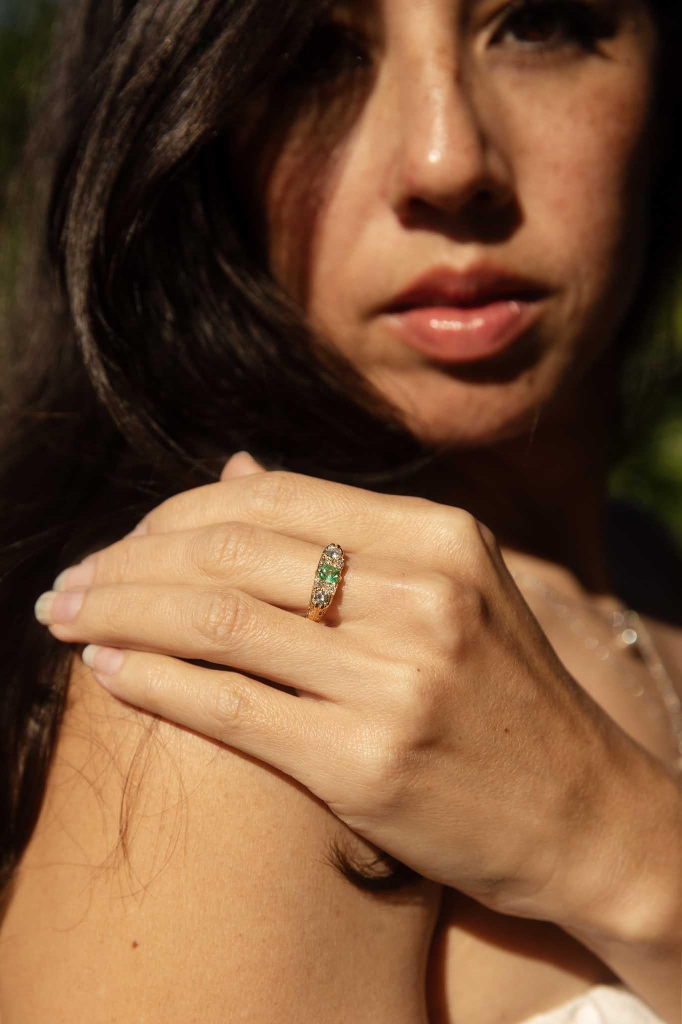 A radiant queen with a heart full of vintage allure, The Jamie Ring is a captivating jewel. Crafted in 18 carat gold, her vibrant emerald heart beats at the center of a shimmering diamond court. They embrace her with delicate ribbons of gold,
