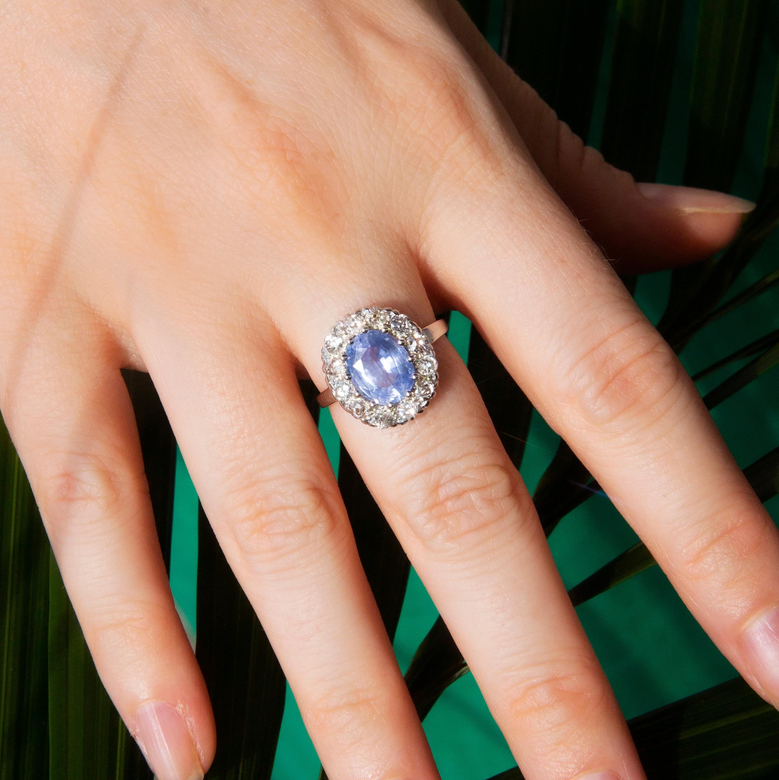 Dieser wunderschöne Ring aus den 1950er Jahren ist aus schimmerndem Platin geschmiedet und zeigt einen hellblauen, oval geschliffenen Saphir im Ceylontyp mit einem schimmernden Halo aus zwölf runden Diamanten im Brillantschliff. Sie hatte den Namen