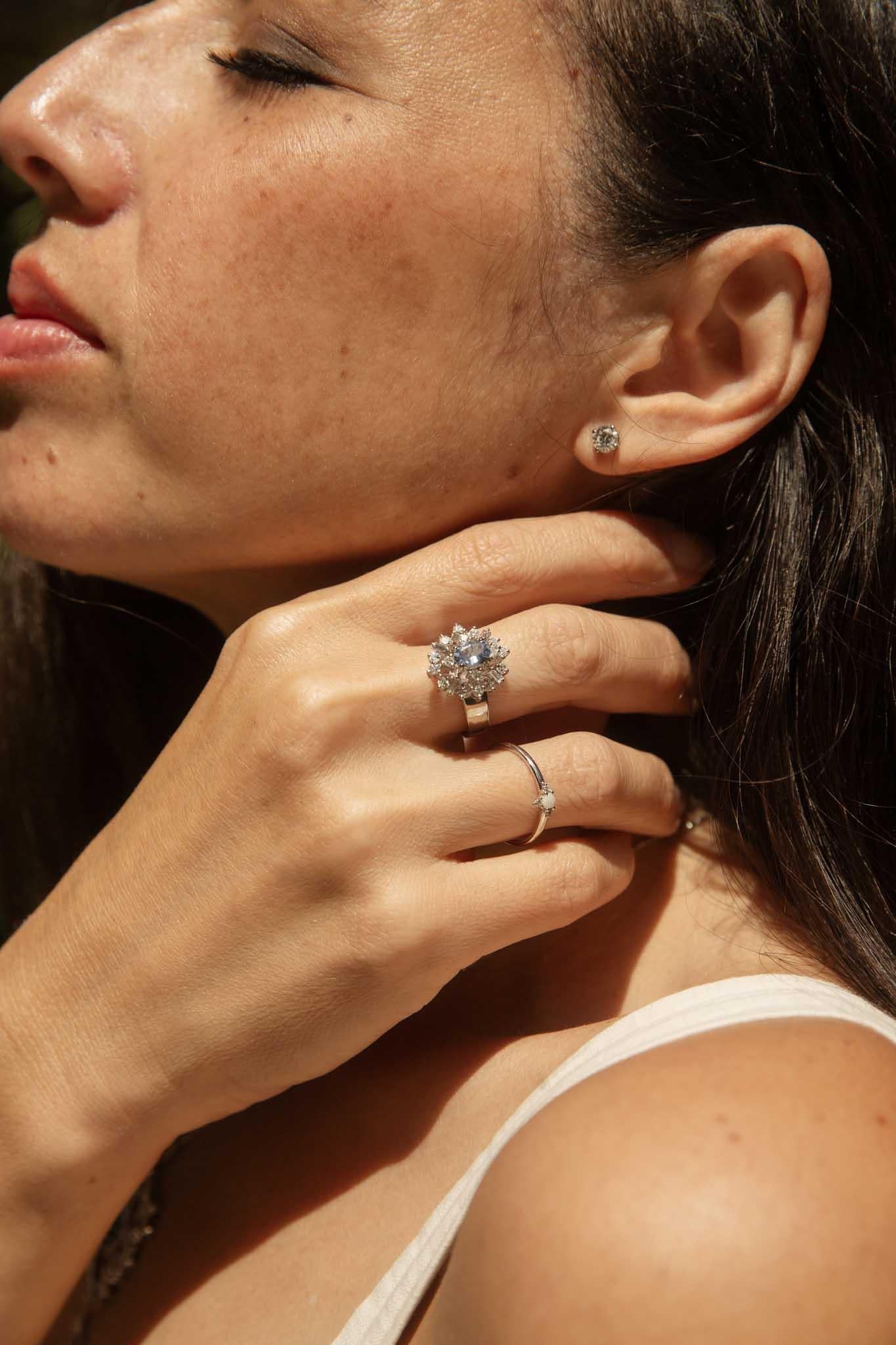 Dieser Ring aus 18-karätigem Weißgold fängt den Glanz eines Wintermorgens ein und zeigt einen blauen Ceylon-Saphir, der von einem strahlenden Cluster aus runden und Baguette-Diamanten umgeben ist. Der zarte Farbton des Saphirs erinnert an die Ruhe