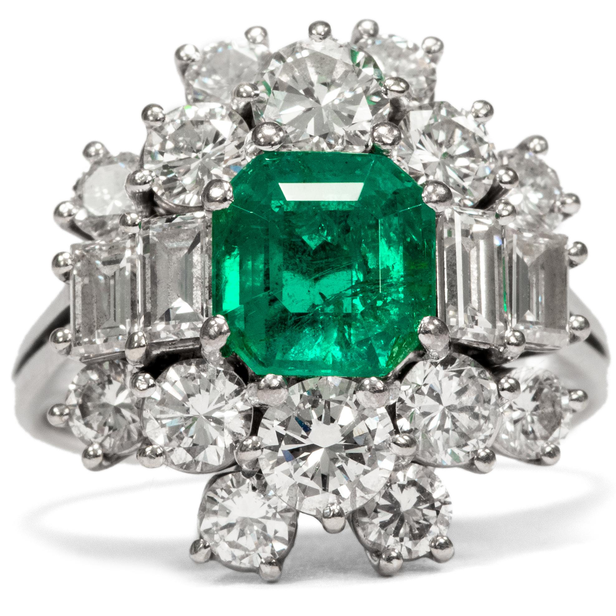 This exquisite ring is a creative interpretation of the classic cluster ring. At its centre is a luminous green emerald, beautifully clear and weighing 1.30 ct. 18 diamonds in brilliant and baguette cuts surround the central gemstone, weighing 2.57