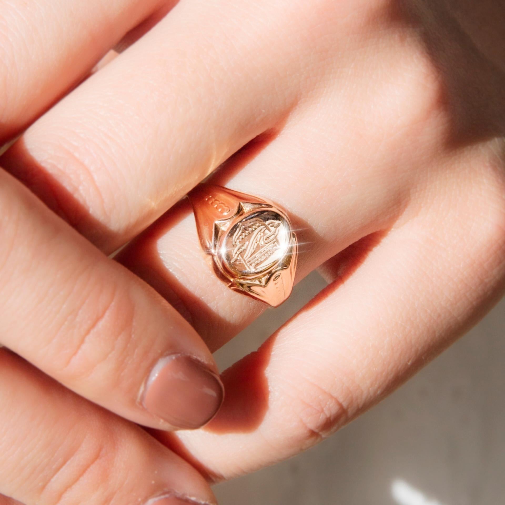 Forged in 14 carat rose gold, this darling signet ring features pleated and patterned shoulders widening into a flat oval top with the intricately engraved letters 