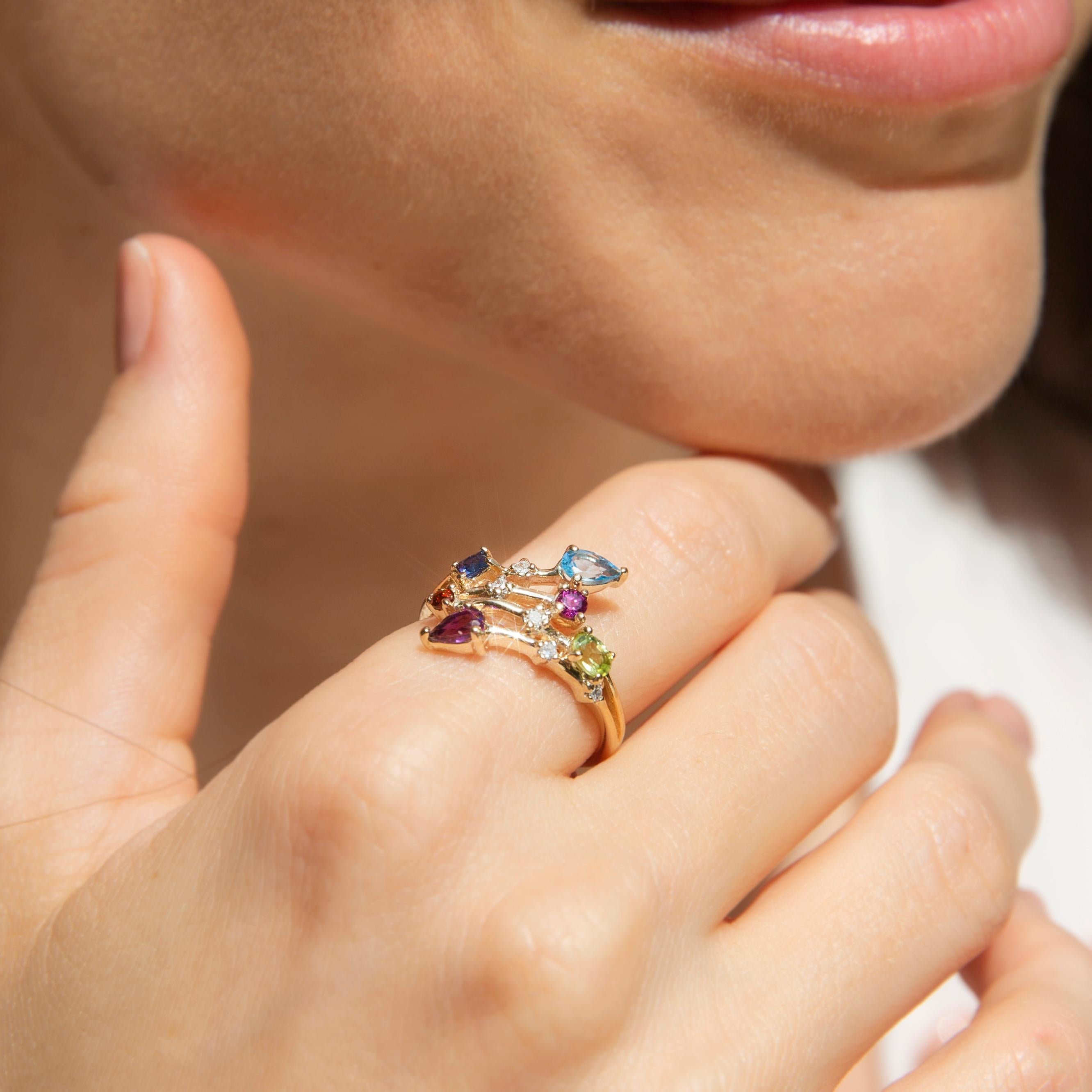 Forged in 9 carat yellow gold, this gorgeous band features split crossover shoulders holding a plethora of accent stones - one pear-shaped amethyst and blue topaz, one oval peridot, one square sapphire, one round rhodolite garnet, one round