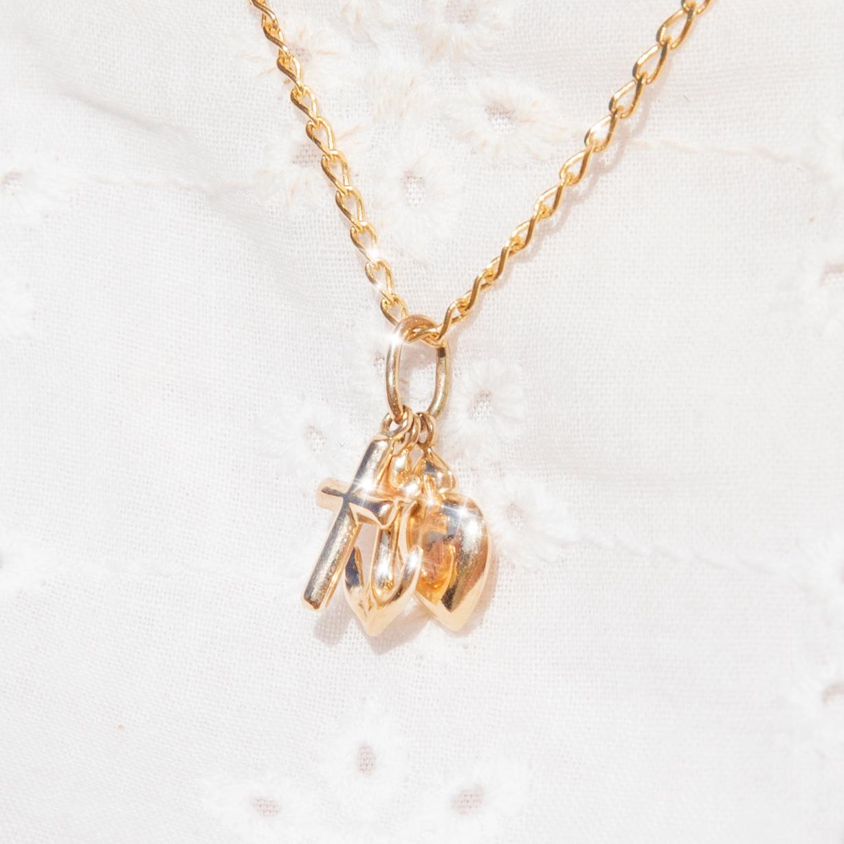 Forged in 9 carat yellow gold, this whimsical vintage piece, circa 1980s, features three pendants - a heart, a cross, and an anchor - threaded on a fine 9 carat gold curb-link chain. We have named this darling piece The Nyra Pendants & Chain. Her