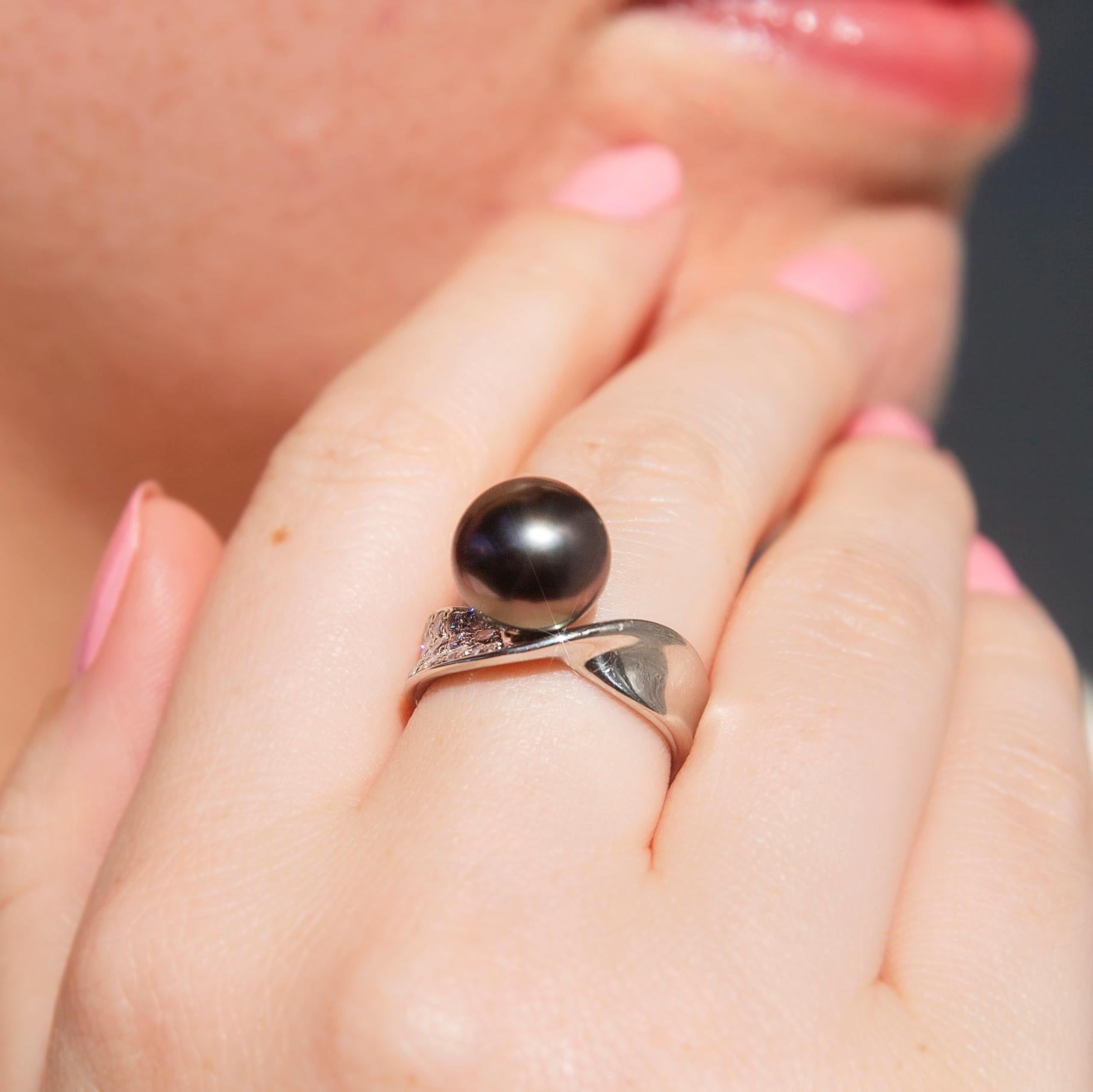 Lovingly crafted in platinum, this enchanting vintage ring, circa 1980s, features a flat band with a twisting ribbon band encrusted on one side with round brilliant cut diamonds and a stunning dark silvery-grey Tahitian pearl set at the top. Her