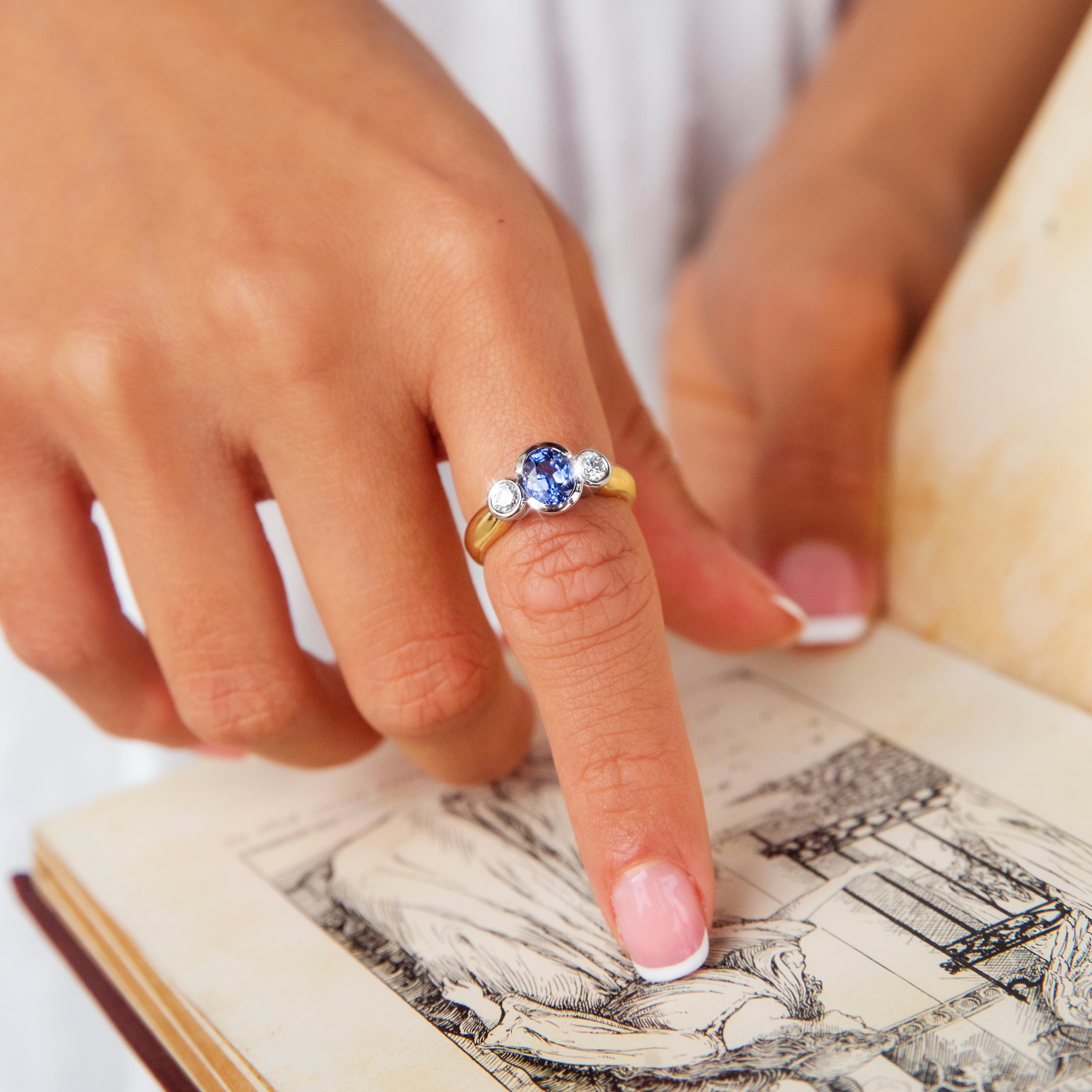 Forged in shimmering 18 carat gold, this delightful vintage 1990s ring features a white gold bezel setting holding one gorgeous light blue Ceylon type sapphire flanked by a duo of shimmering round brilliant cut diamonds atop a high polish yellow