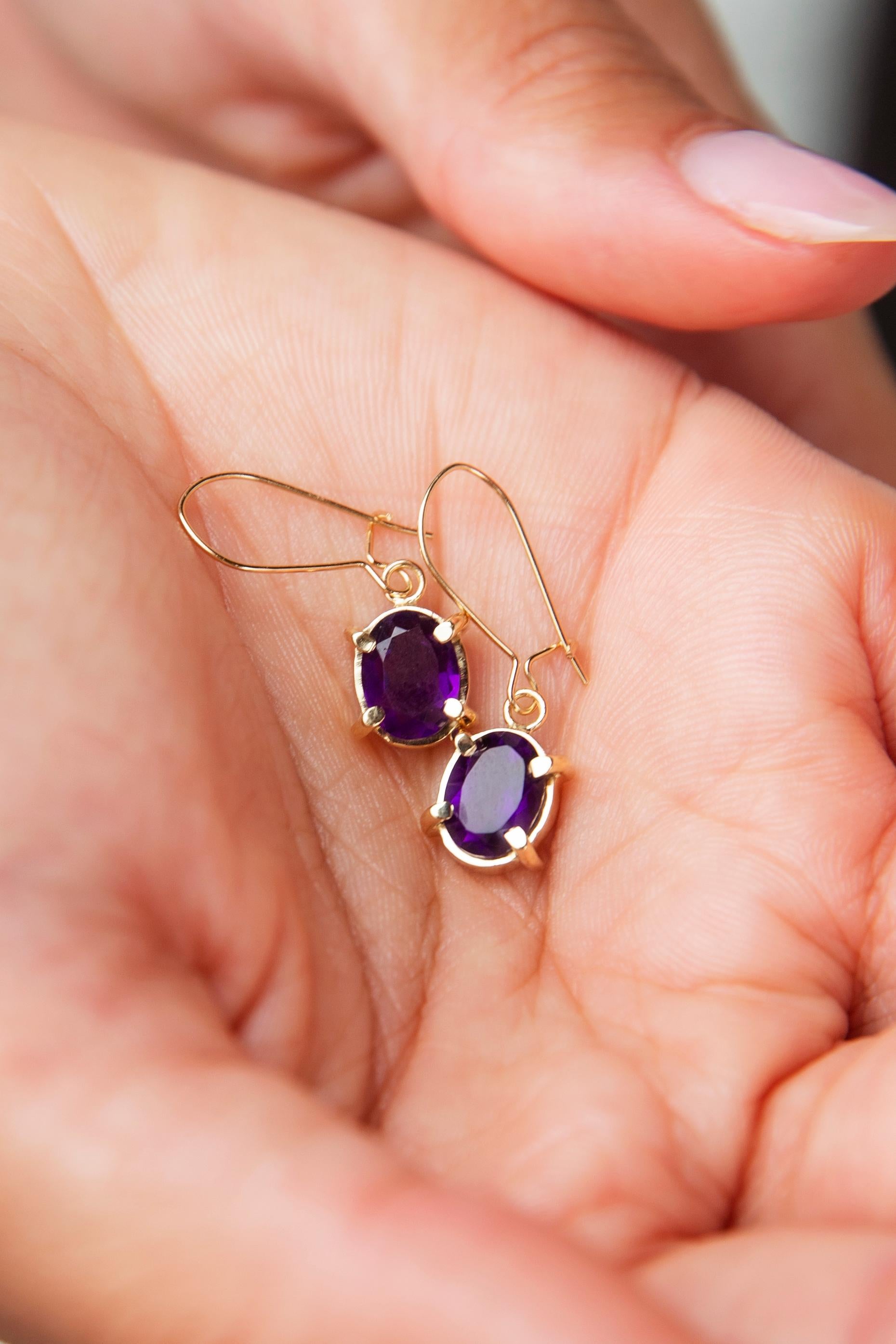 Crafted in 18 carat yellow gold, these vintage drop earrings, circa 1990s, each feature a lovely oval cut purple amethyst in a claw setting and are finished with continental hook backings for easy and comfortable wear. We have named these adorable