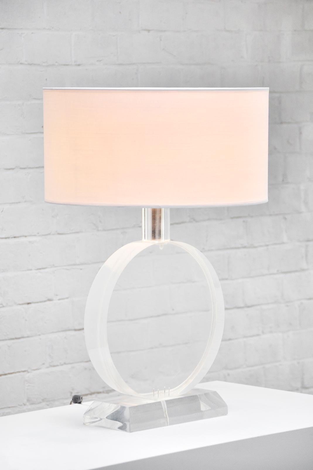 Unique sculptural and large Karl Springer style desk or table lamp made of solid heavy lucite. The lamp body is circle shaped and sitting on top of a chunky rectangular lucite base. Topped with a white cotton shade. Very good vintage condition,