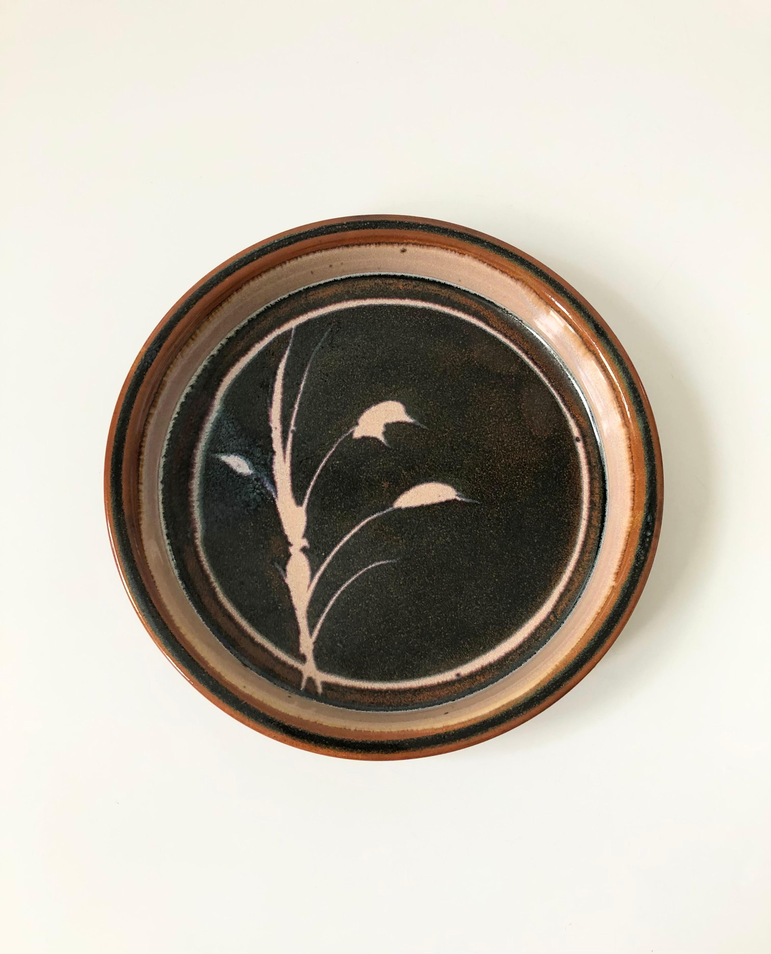 A vintage circular studio pottery tray. Nice large size, perfect for using as a serving dish or centerpiece. Features an offset handpainted wheat design in earthy muted purple and brown glazes. Signed on the base.
  