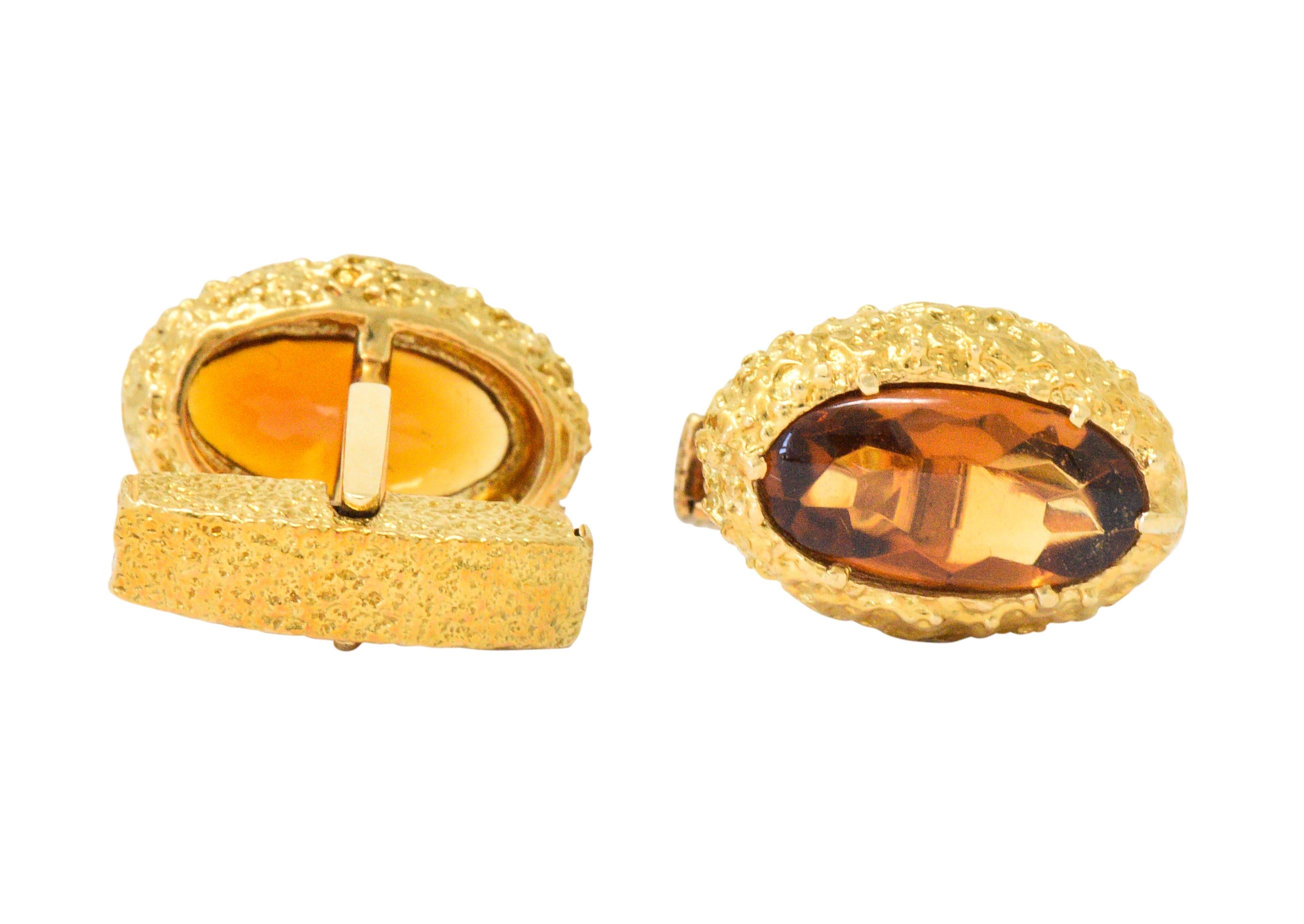 Lever back style cufflinks featuring buff top citrine, measuring approximately 16.0 mm x 8.0 mm

Transparent with a faceted base and a well-matched deep cognac color

Bezel set in a highly textured surround

With maker's mark

Tested as 18 karat
