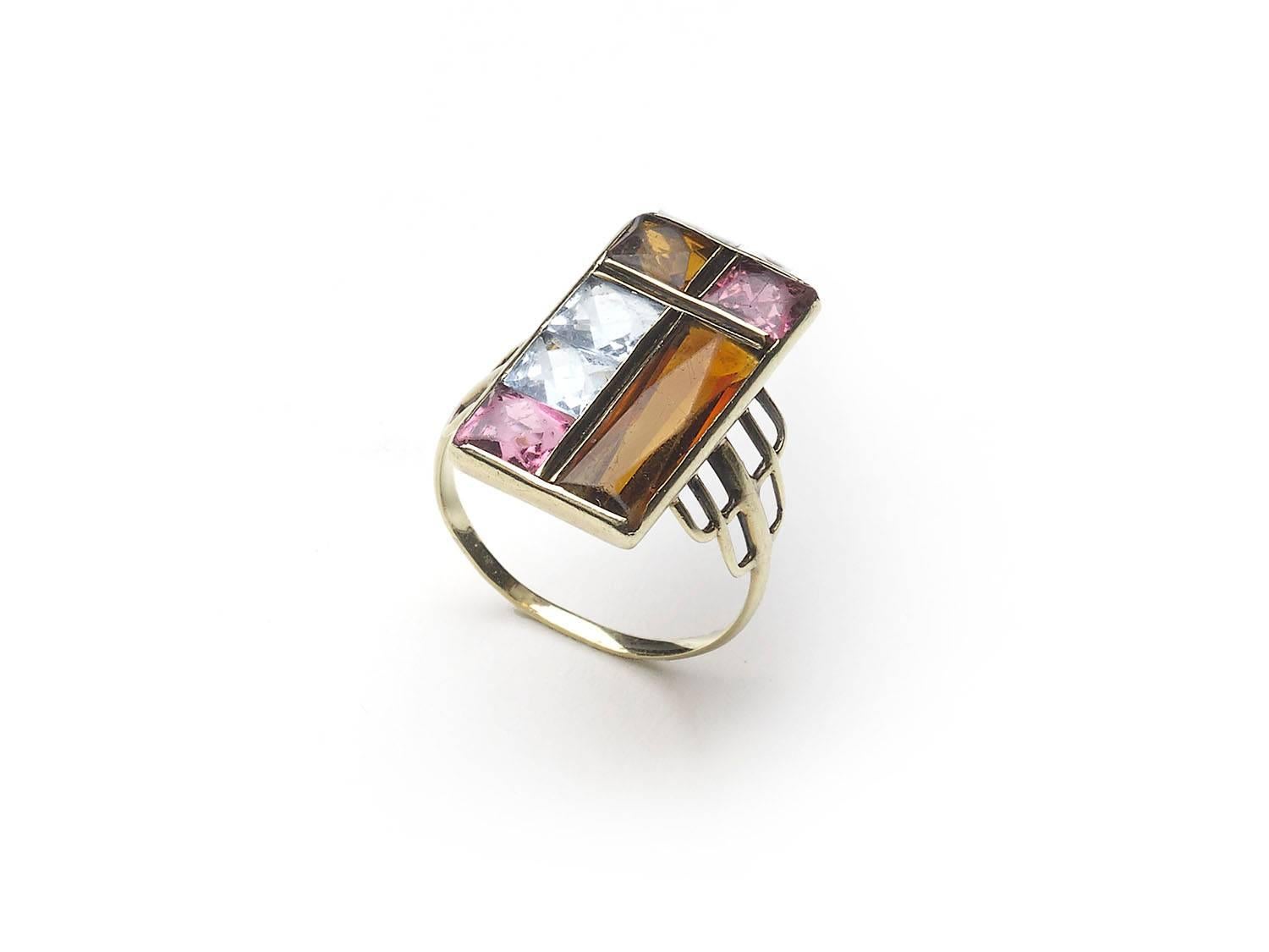 A vintage multi gem ring, set with two princess-cut aquamarines, two princess-cut pink tourmalines, a princess-cut Madeira citrine, and a rectangular, faceted Madeira citrine, set in channel and rub over settings, in an abstract, modernist design,