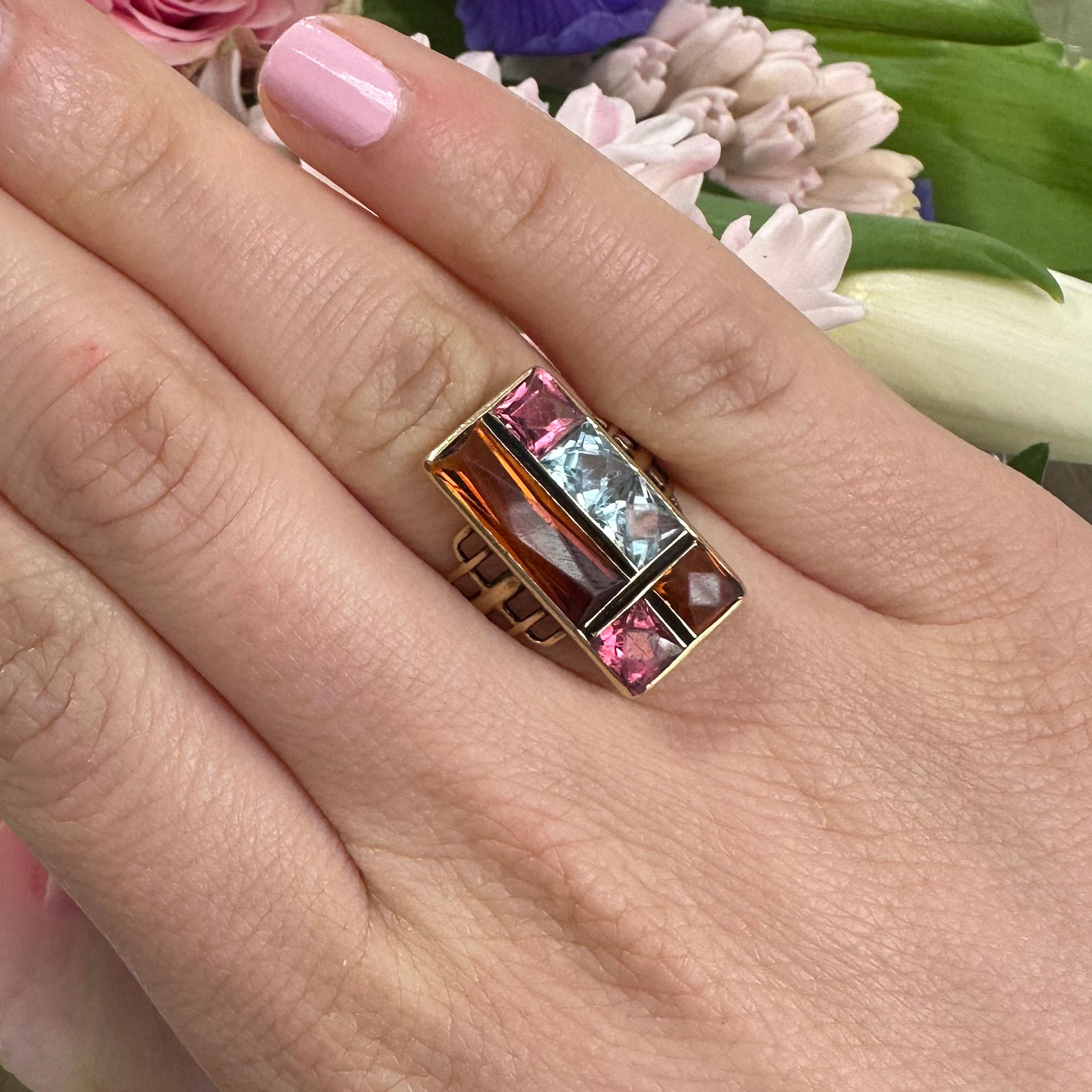 A vintage multi gem ring, set with two princess-cut aquamarines, two princess-cut pink tourmalines, a princess-cut Madeira citrine, and a rectangular, faceted Madeira citrine, set in channel and rub over settings, in an abstract, modernist design,