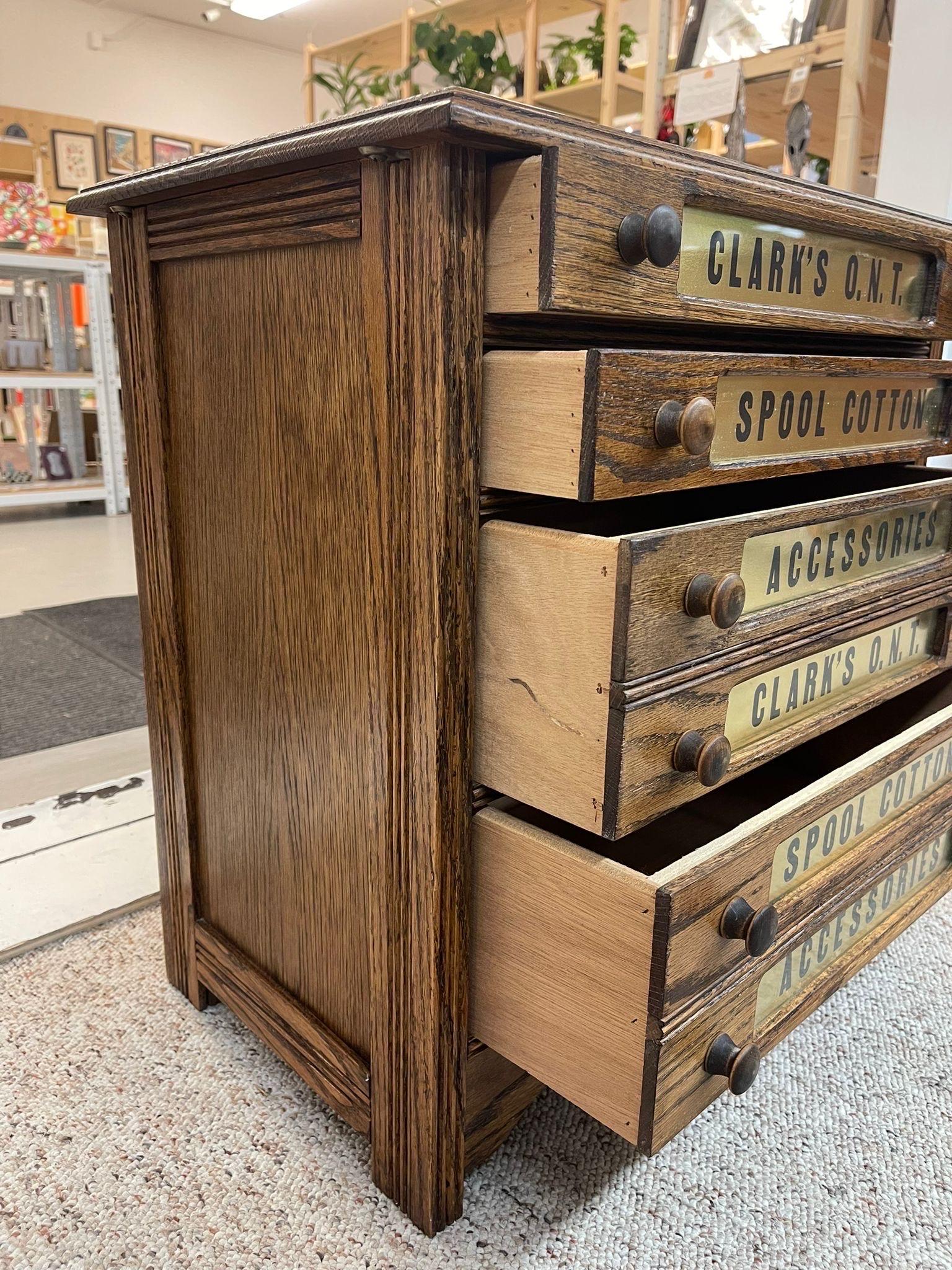 walnut Toned 4 Drawer Spool Cabinet. Wooden Handles with Brass Toned Labels on the Drawers. Lower 2 Drawers are Larger in Size. Thread Pictured is Included with the Sale of the Cabinet. Vintage Condition Consistent with Age as Pictured. 