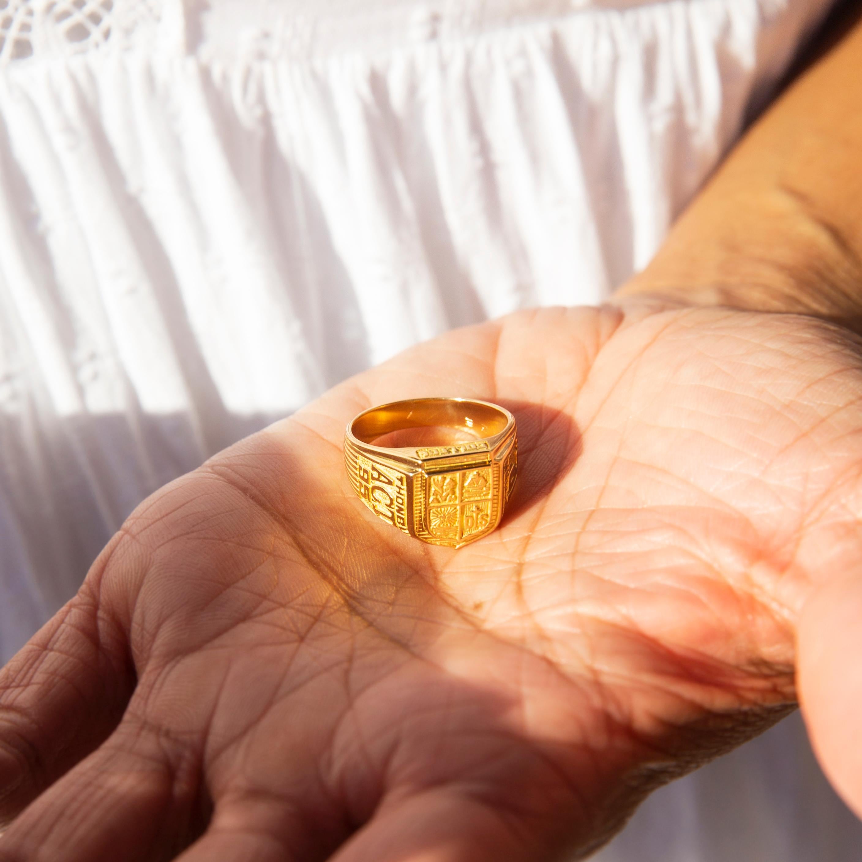 Dieser klassische Graduierungsring ist aus 18 Karat Gold geschmiedet und verfügt über ein kompliziertes, in vier Abschnitte unterteiltes Wappen mit jeweils einem symbolischen Motiv und feierlichen Graduierungssymbolen auf jeder Seite des gerillten