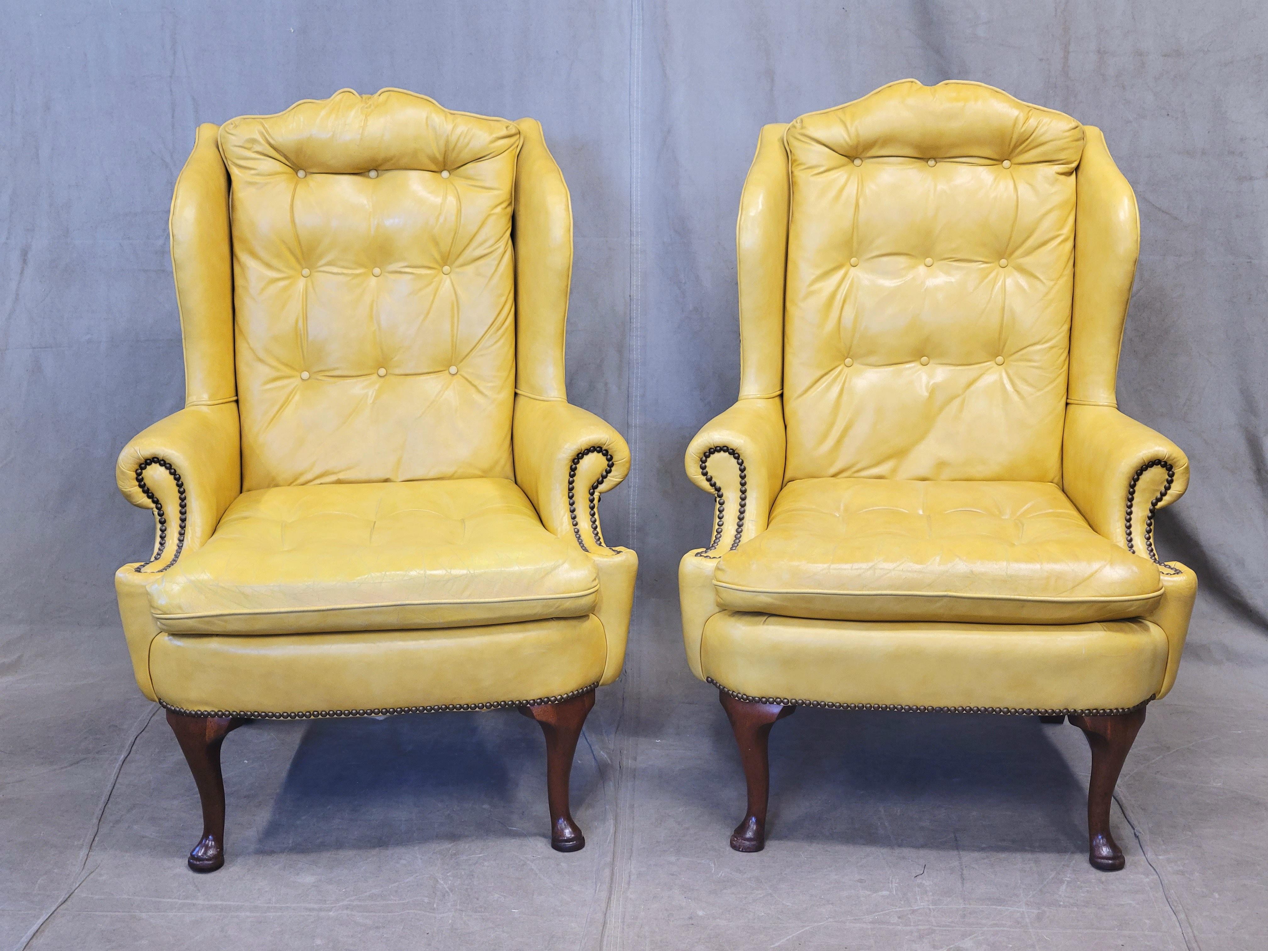 Une magnifique paire de fauteuils à oreilles Chesterfield jaunes vintage avec des têtes de clous en laiton, accompagnés de coussins lombaires en duvet botanique noir personnalisés. Les chaises, qui datent probablement des années 1970, sont en cuir