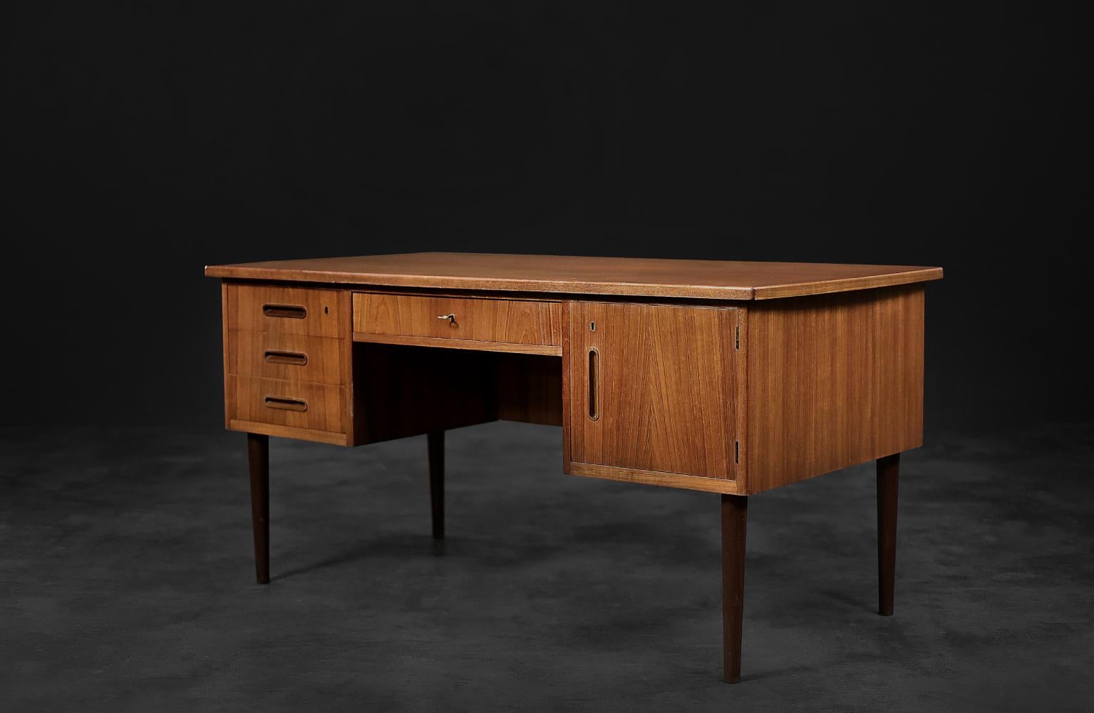 This large, bilateral desk was made in Denmark during the 1960s. It is finished in teak wood in a warm shade of brown. It has a balanced design, where style and functionality go hand in hand. The front consists of a block of three drawers, one