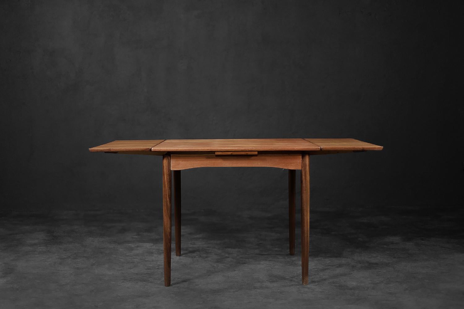 This classic dining table was made in Denmark during the 1960s. The table is an example of Danish minimalism from the Mid-century Modern era. It is made of teak wood in a natural shade of brown. It has turned legs made of solid wood. Due to the