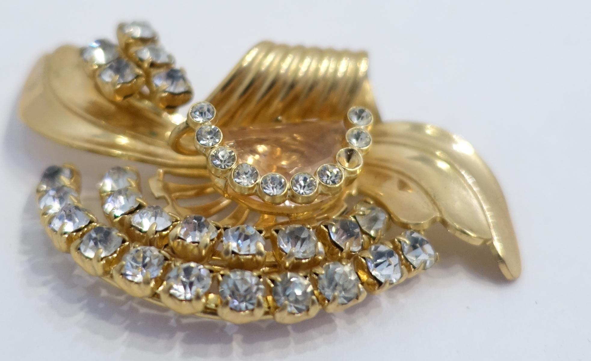 This vintage brooch has a retro design.  It has clear crystals going throughout its gold tone wavy body.  In excellent condition, this brooch measures almost 3” x 1-3/4”.