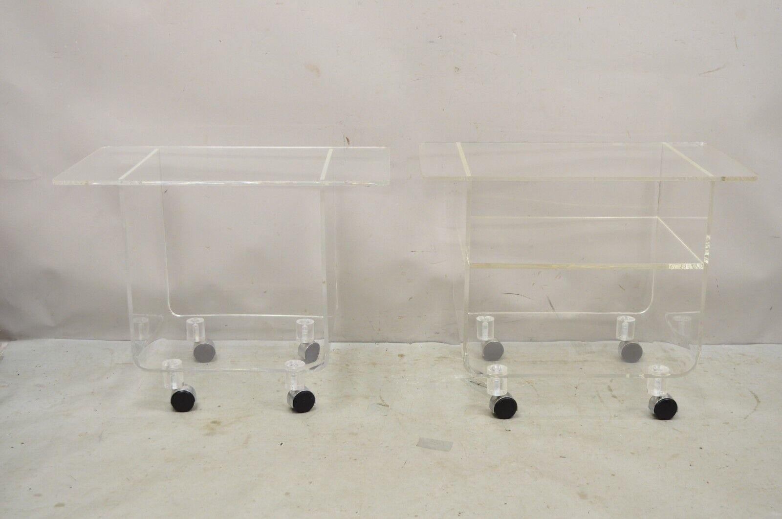 Vintage Clear Lucite Acrylic Mid Century Modern Rolling Side Tables - Complimentary Pair. Item featured is a slight variation in style and size. One table has a middle shelf while the other is open. Size between tables varies slightly. Please see