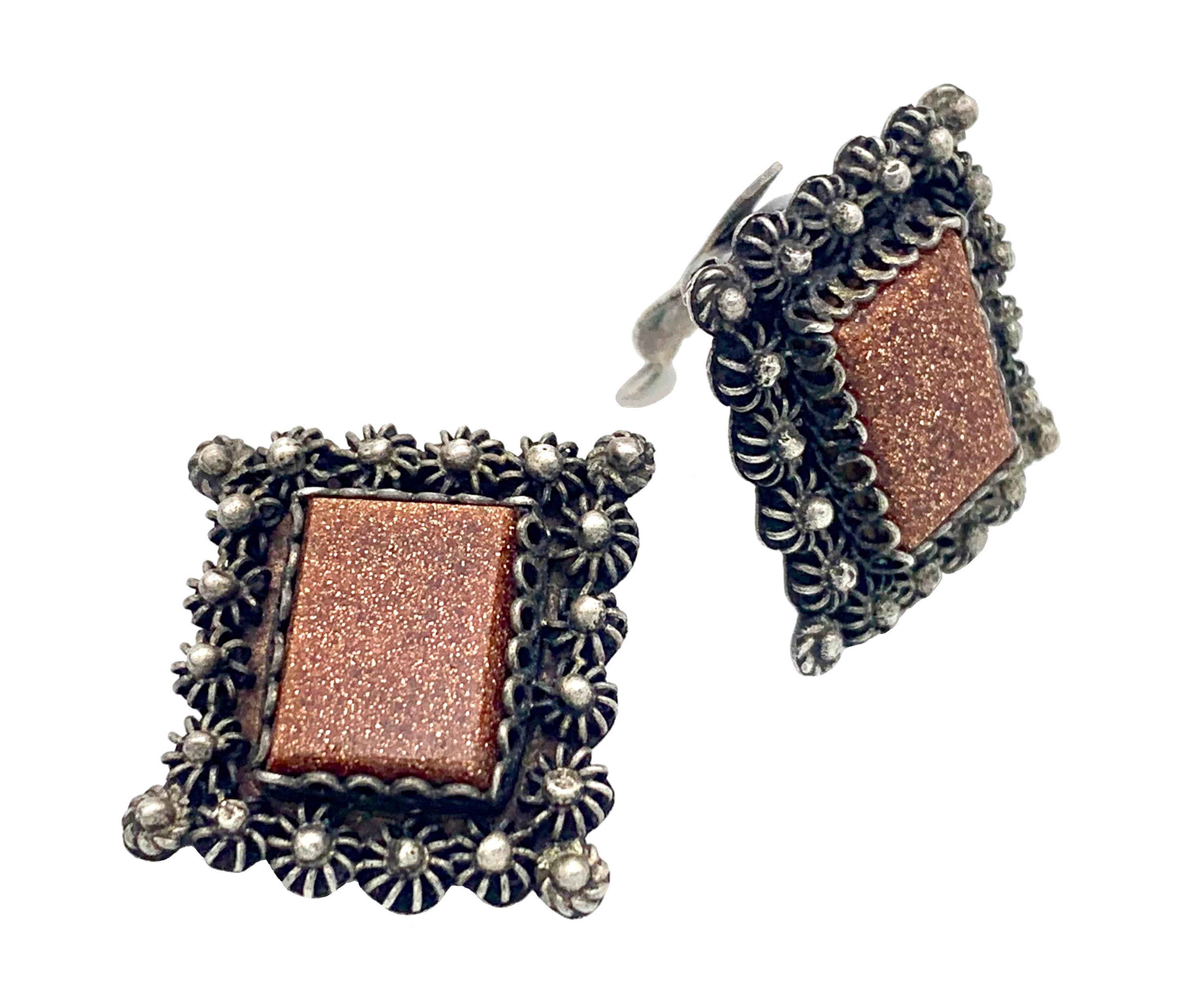 The clip on earrings were handcrafted out of silver in the mid-20th century. 
The rectangular aventurine glass plaques are framed by raised elements made out of silver wire and granulation. The earrings bear silver marks.
