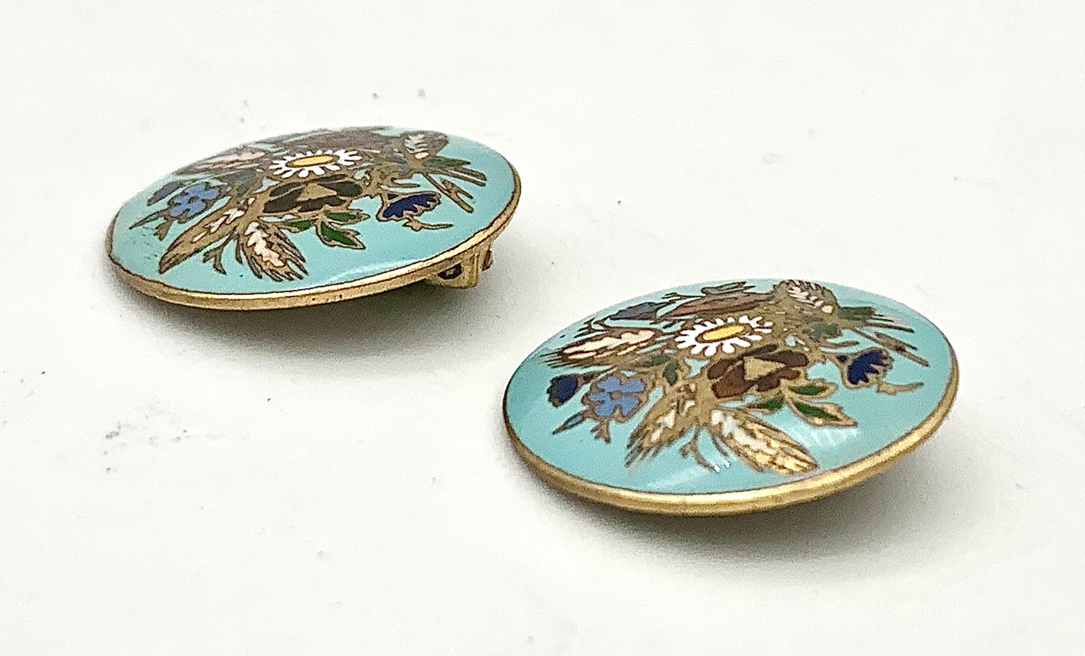The enamel paintings on these clip-on earrings are celebrating summer. We see colourful bouquets made up from red, blue, pale blue and white flowers together with oars painted in enamel on a gold ands turquoise background.  the ear clips and ear