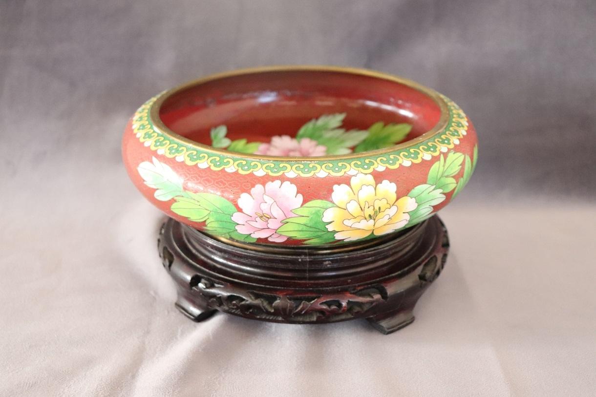 Beautiful Vintage cloisonne bowl from China, with carved teak stand, circa 1980s. The bowl has a rust red background with an overall pattern of clouds made from brass wire and flowers. The designs also include a bluebird, both on the side and inside