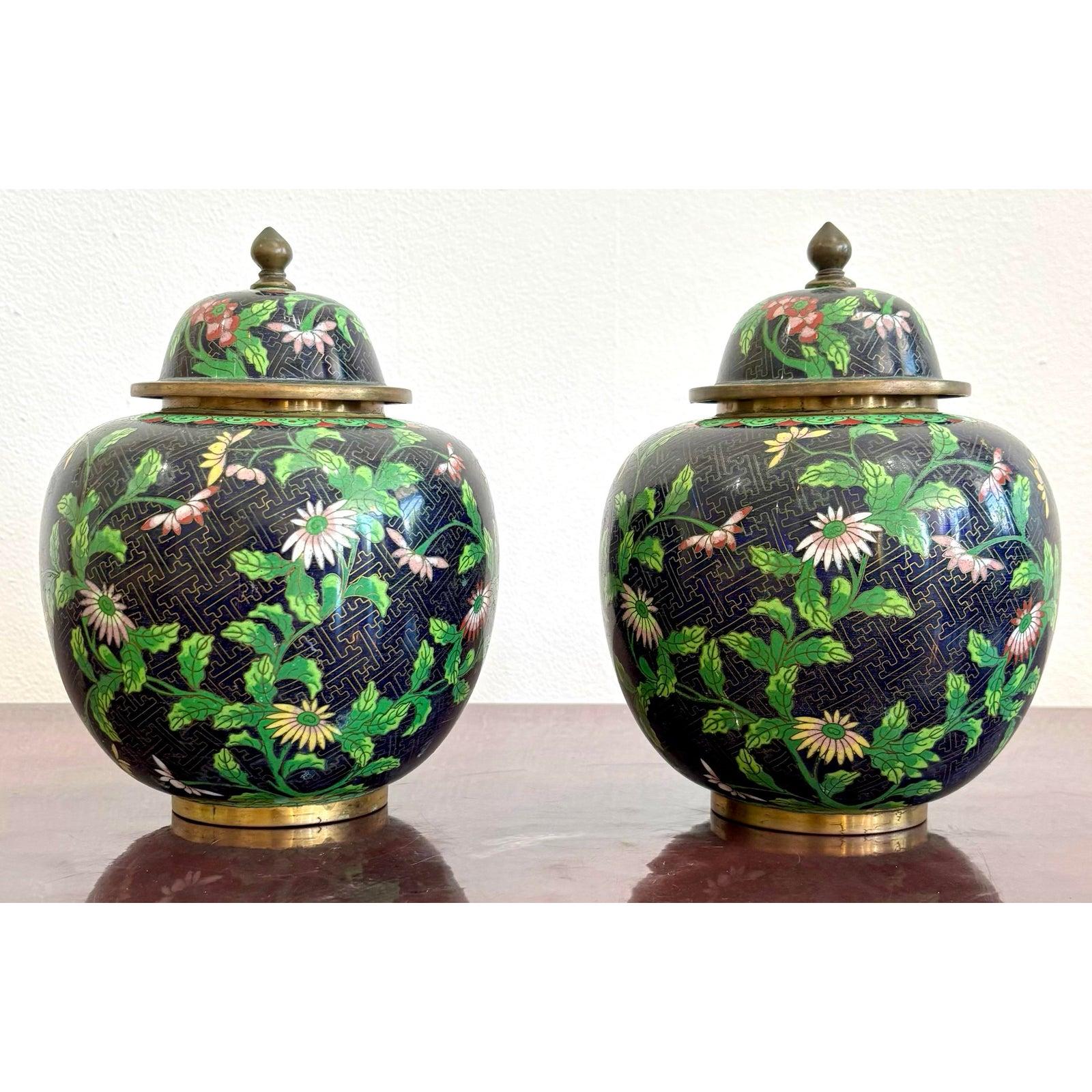 This vibrant pair of lidded cloisonné jars is a striking example of traditional craftsmanship and decorative artistry. Set against a deep navy enamel background, delicate floral vines and fluttering butterflies dance across the surface in vivid