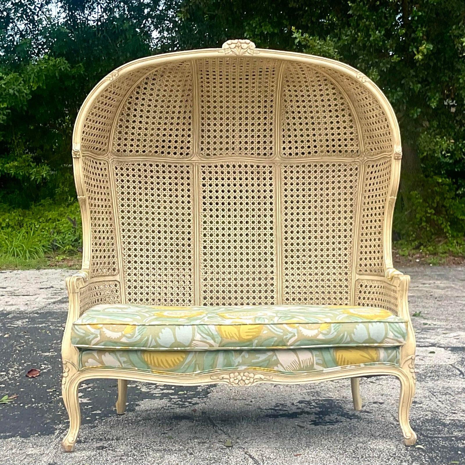A stunning vintage Boho loveseat. The iconic balloon back shape with inset cane panels. Newly upholstered in a chic floral printed linen cotton blend. The 2 throw pillows are included. Acquired from a Palm Beach estate