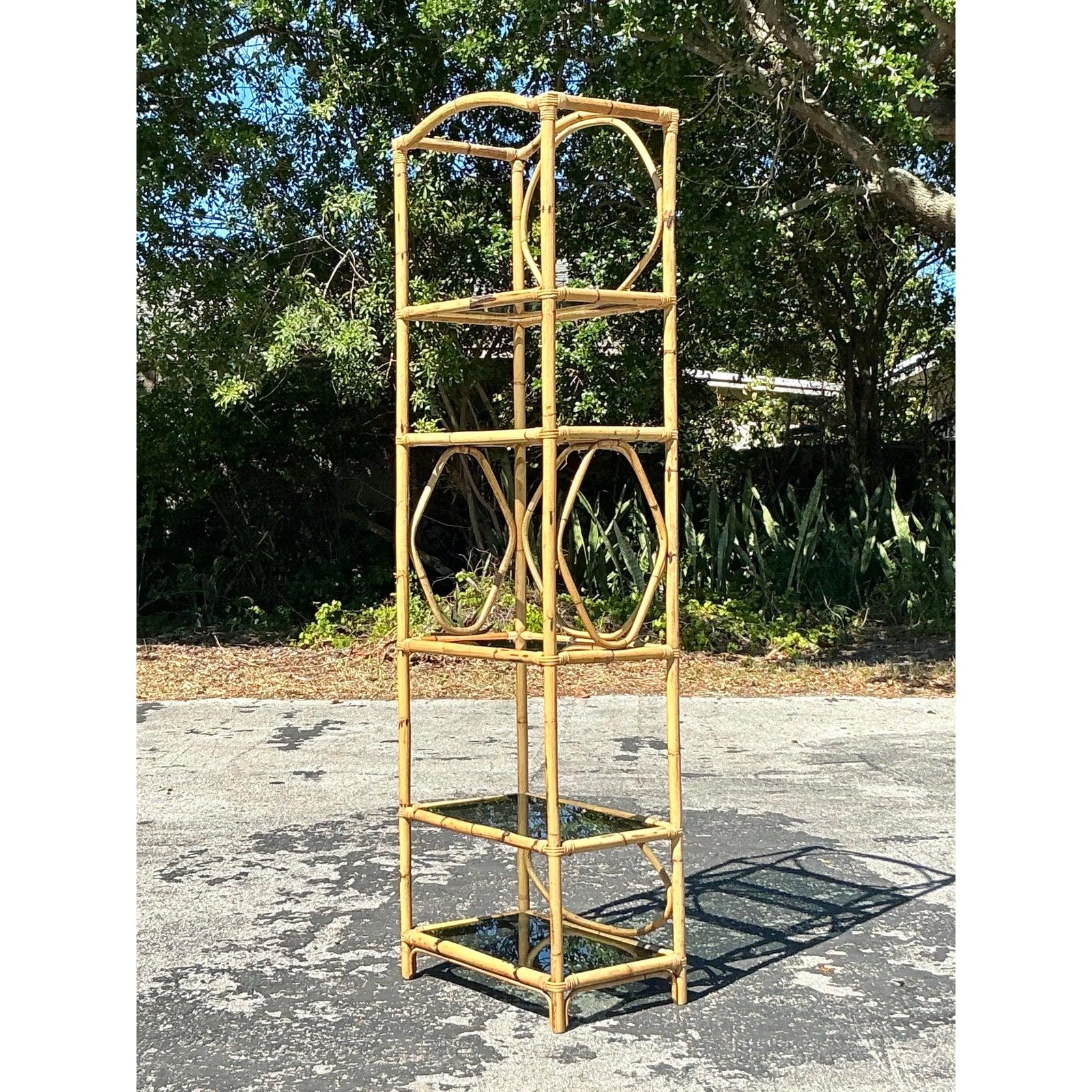 Tropische Eleganz mit dieser auffälligen, hohen Vintage-Etagere aus natürlichem Bambus. Die hoch aufragende Silhouette mit ihren kreisrunden dekorativen Aussparungen und getönten Glasböden bietet eine luftige und künstlerische Struktur, die sich