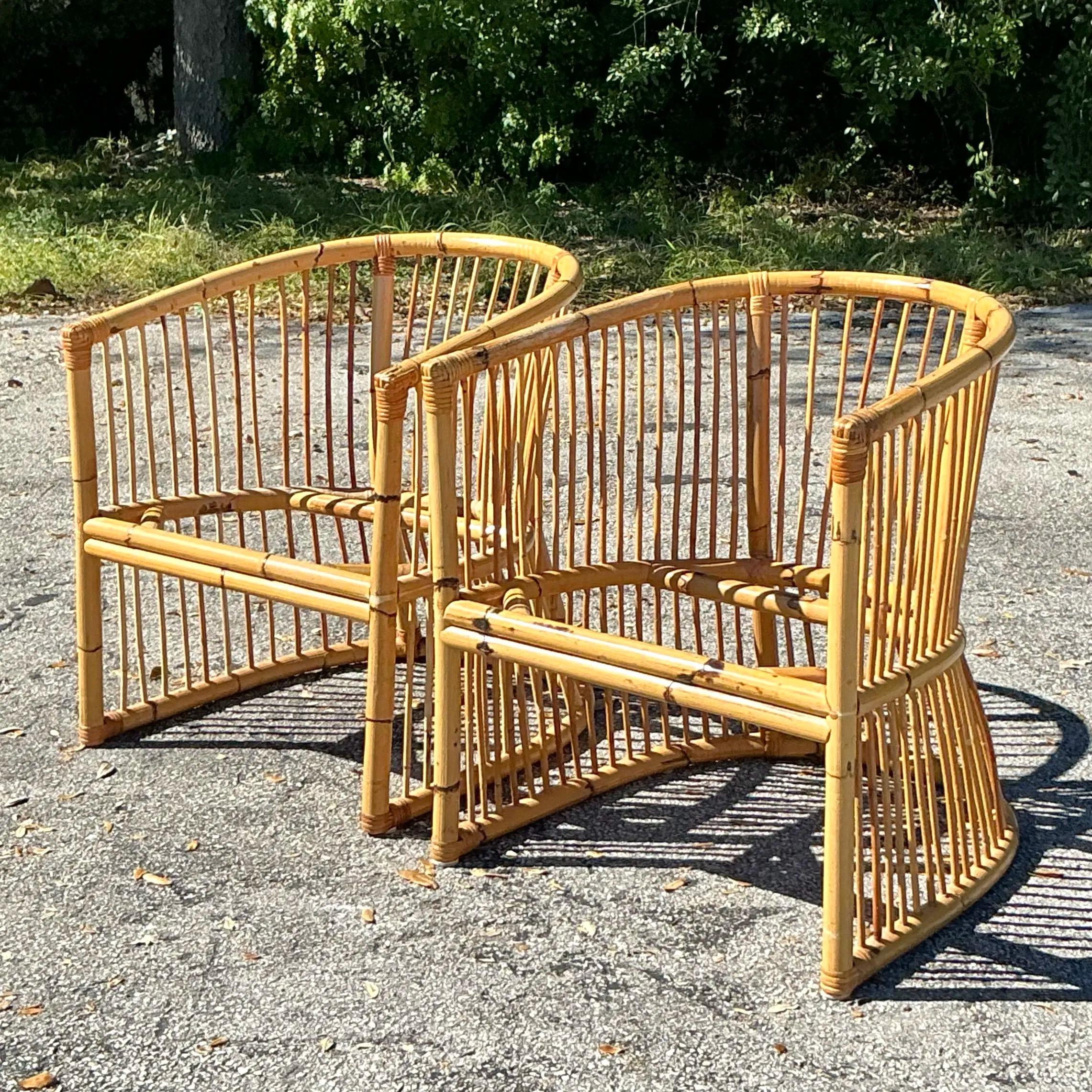 A pair of vintage coastal tub chairs crafted from bamboo, showcasing a rounded silhouette and intricate woven details. These chairs embody a relaxed, tropical vibe with their natural bamboo finish and sturdy construction. Their open framework
