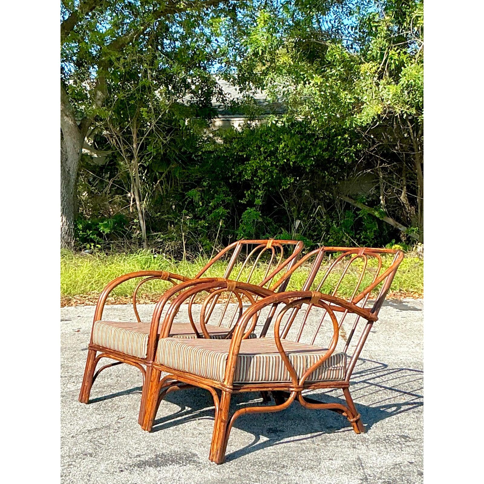Añade un toque de elegancia a tu espacio con este impresionante par de tumbonas vintage de ratán curvado. Con armazones graciosamente curvados y un respaldo de husillo abierto, estas sillas encarnan un relajado encanto costero a la vez que mantienen