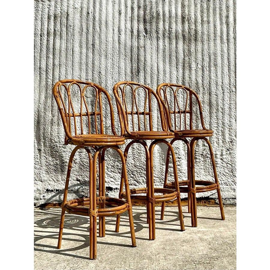 Elevate your home decor with this stunning set of three vintage coastal bent rattan bar stools. These timeless pieces showcase a gracefully curved rattan frame, emphasizing their natural charm and artisanal craftsmanship. Perfectly blending form and