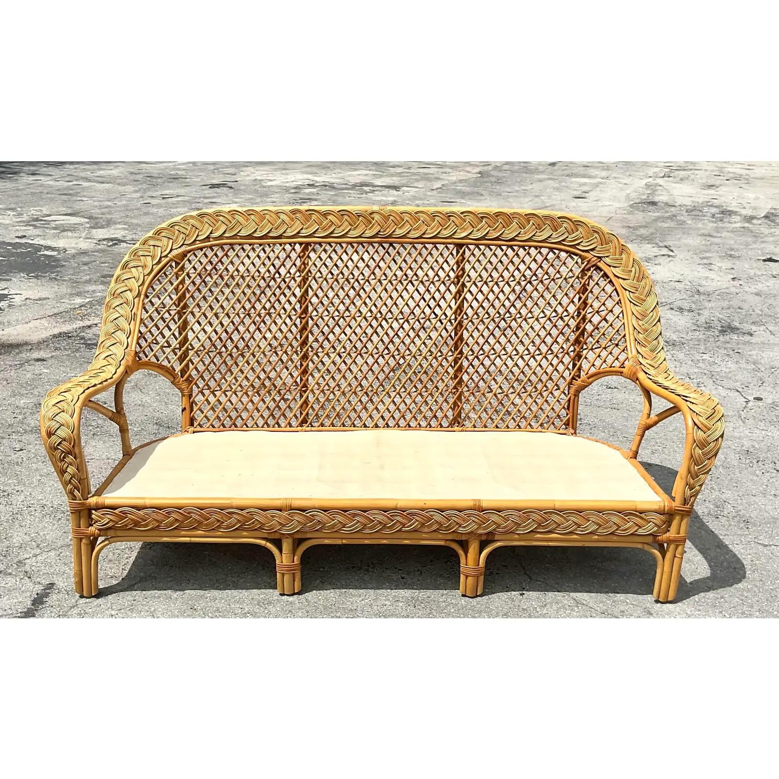 Fantastic vintage Coastal woven rattan sofa. Beautiful braided trim with a high paddle back. Matching loveseat and chairs also available. Cushions included. Acquired from a Palm Beach estate.