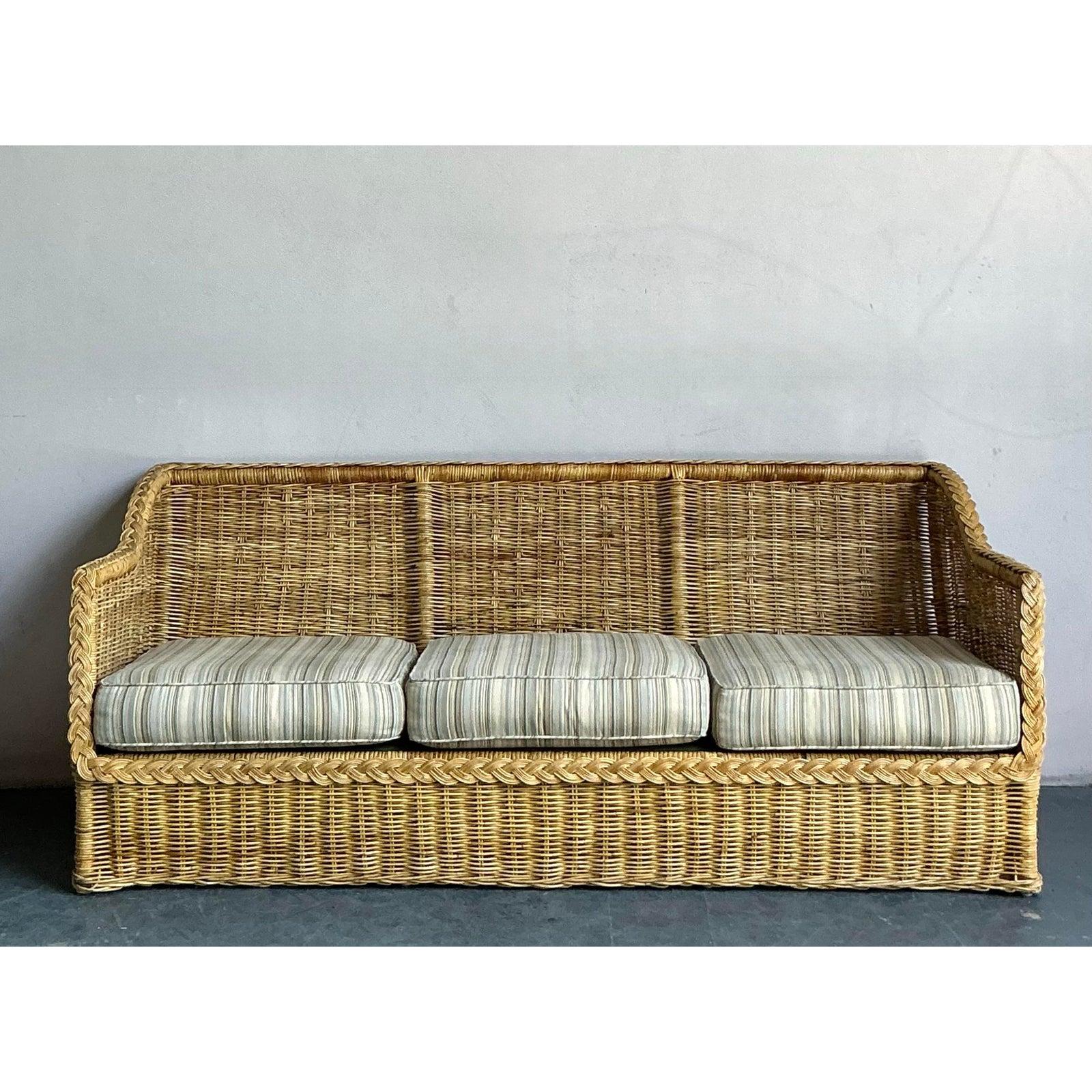 Infunde a tu salón el encanto relajado de este Sofá Vintage Coastal de ratán trenzado, un magnífico ejemplo del diseño bohemio de los años setenta. Este sofá de tres plazas tiene un marco de ratán trenzado a mano, que crea una textura llamativa y
