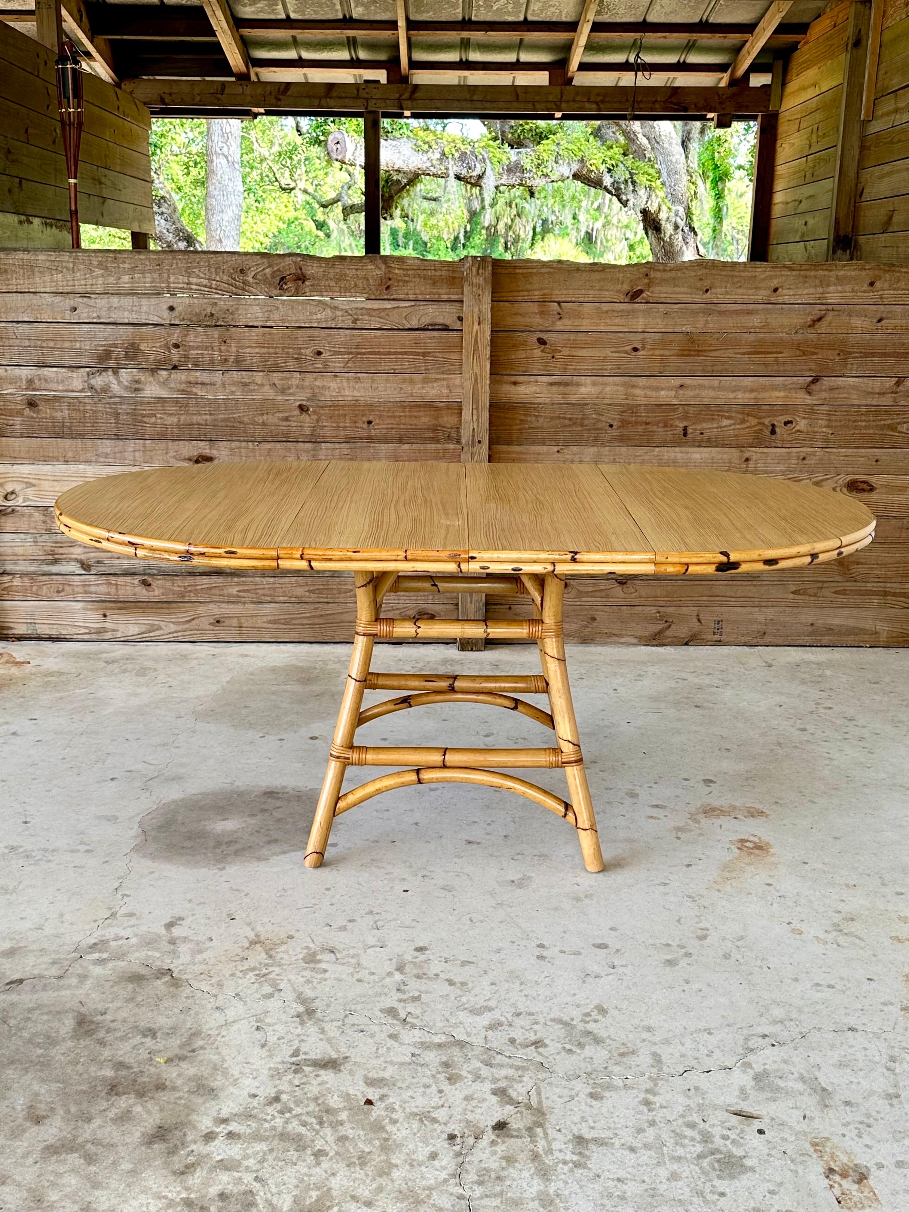 Une table de salle à manger côtière vintage remarquable, fabriquée à partir de bambou brûlé naturel et de rotin, mettant en valeur l'élégance intemporelle de l'île et la chaleur organique. La table est extensible grâce à deux plateaux, ce qui permet