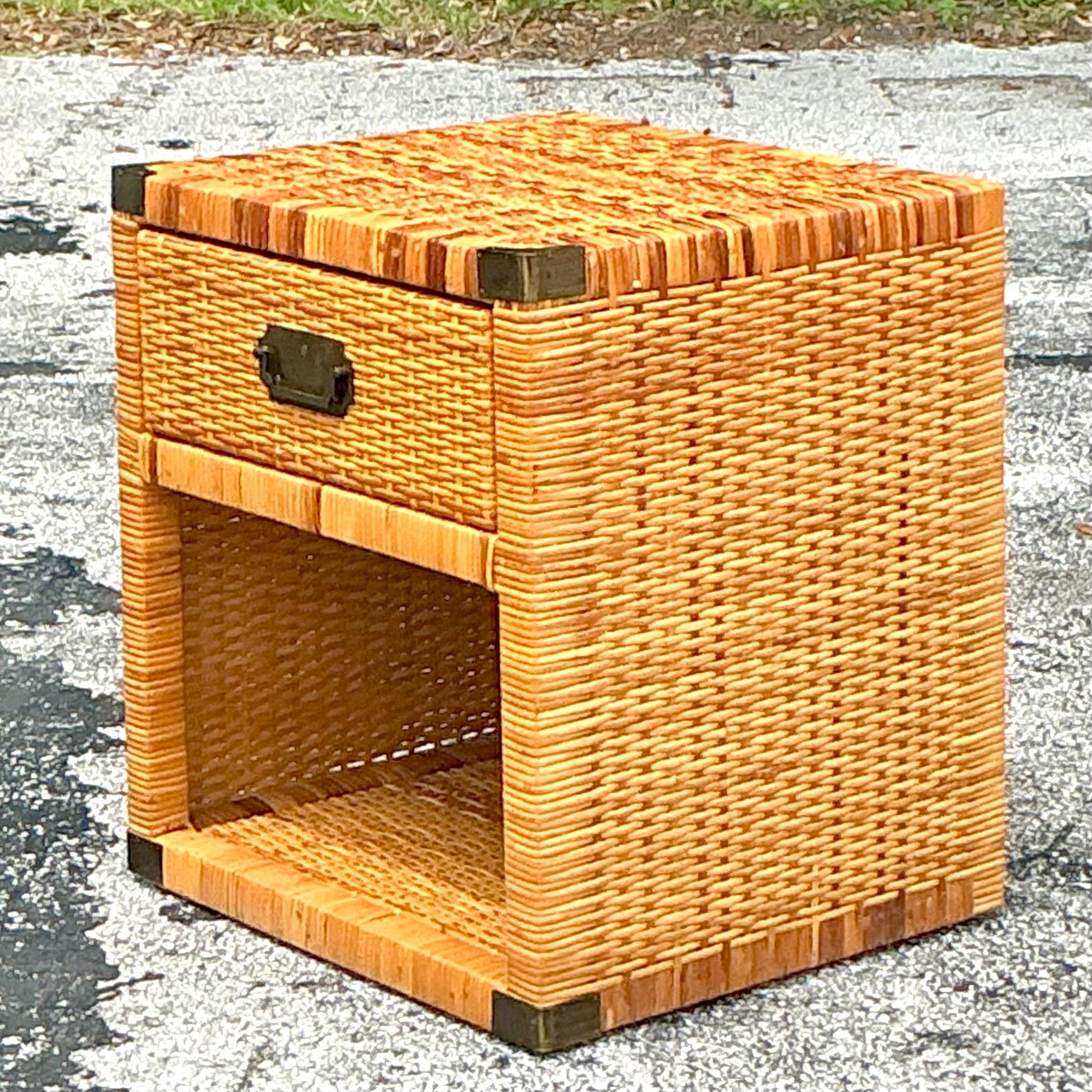 Introduce a touch of seaside elegance to your bedroom with this Vintage Coastal Campaign Woven Rattan Nightstand. Perfect for American-style interiors, this nightstand features the classic Campaign-style brass hardware combined with beautifully
