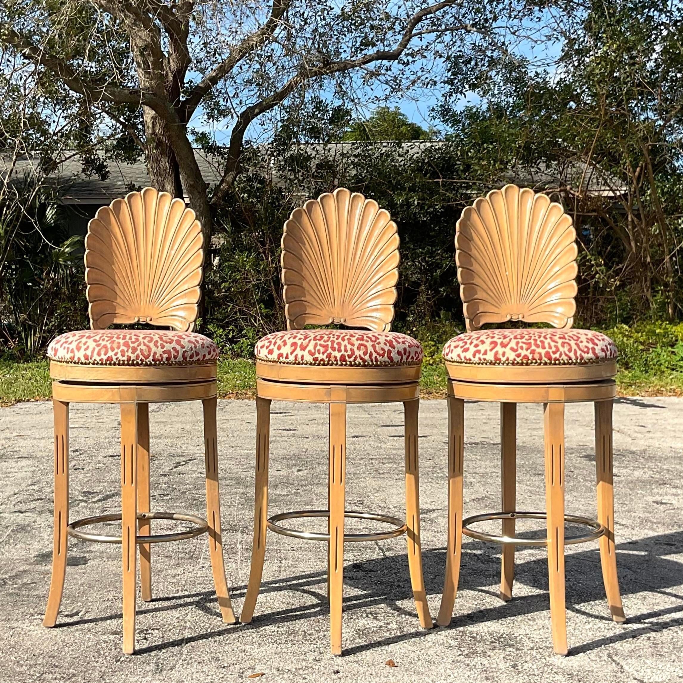 A fabulous set of three vintage Coastal swivel bar stools. A chic hand carved grotto design on tall slender legs. Acquired from a Palm Beach estate.